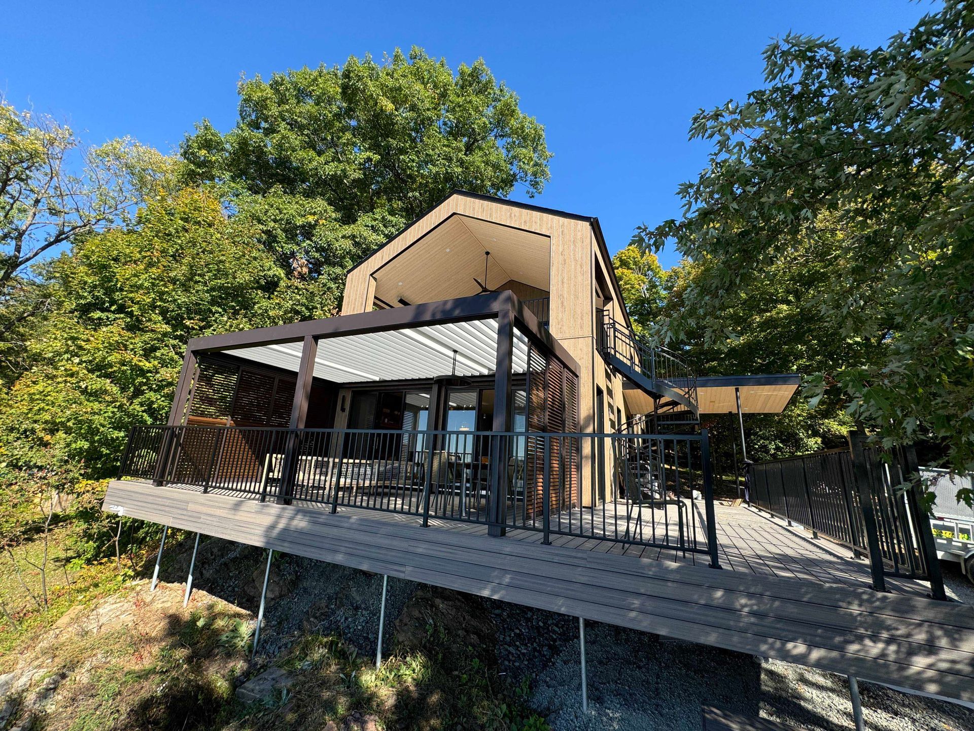 Chalet moderne avec terrasse, entouré d'arbres sous un ciel bleu.