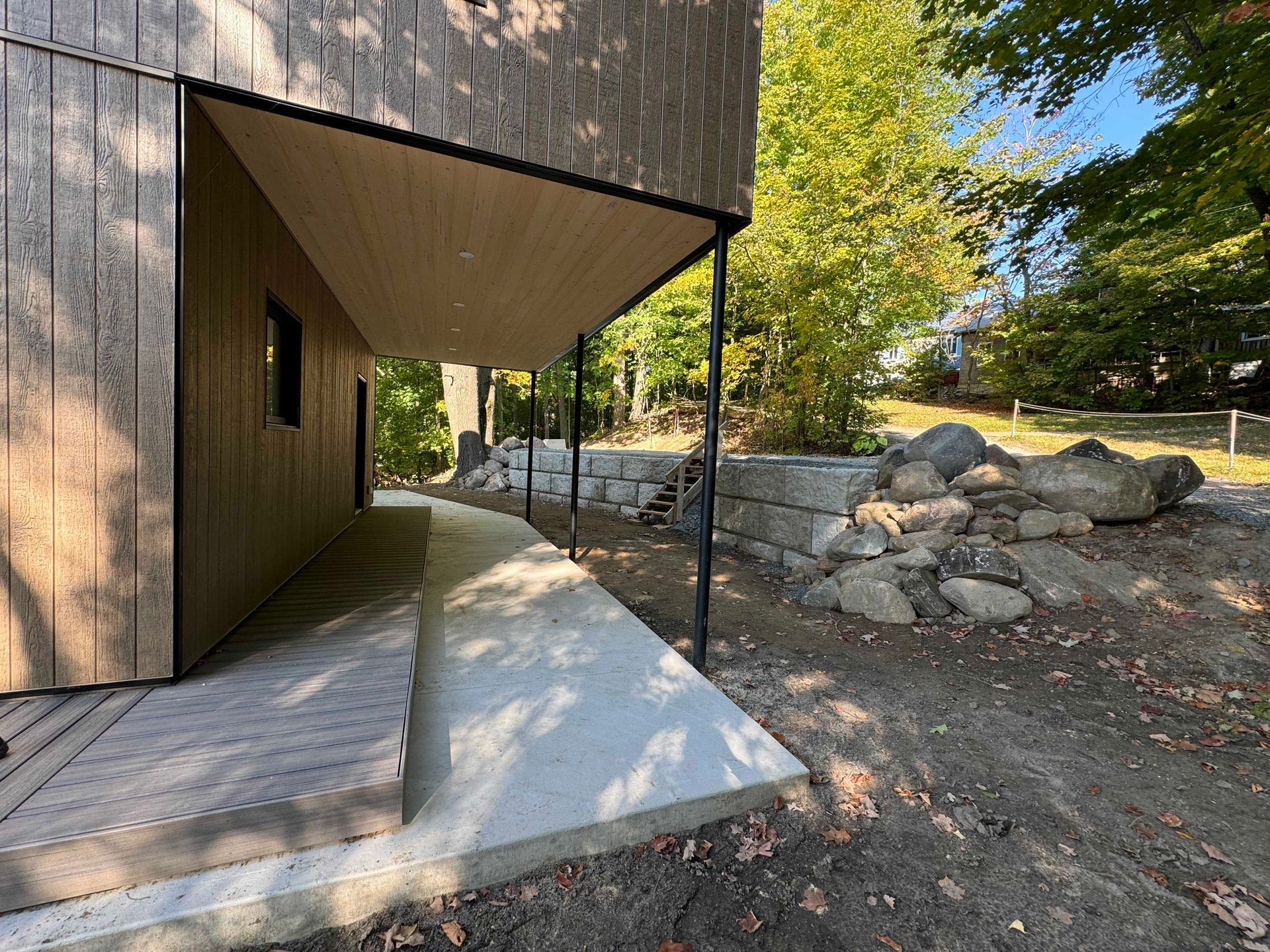 Vue extérieure d'une maison moderne avec une allée en béton, un porche et un mur de soutènement en gros rochers.