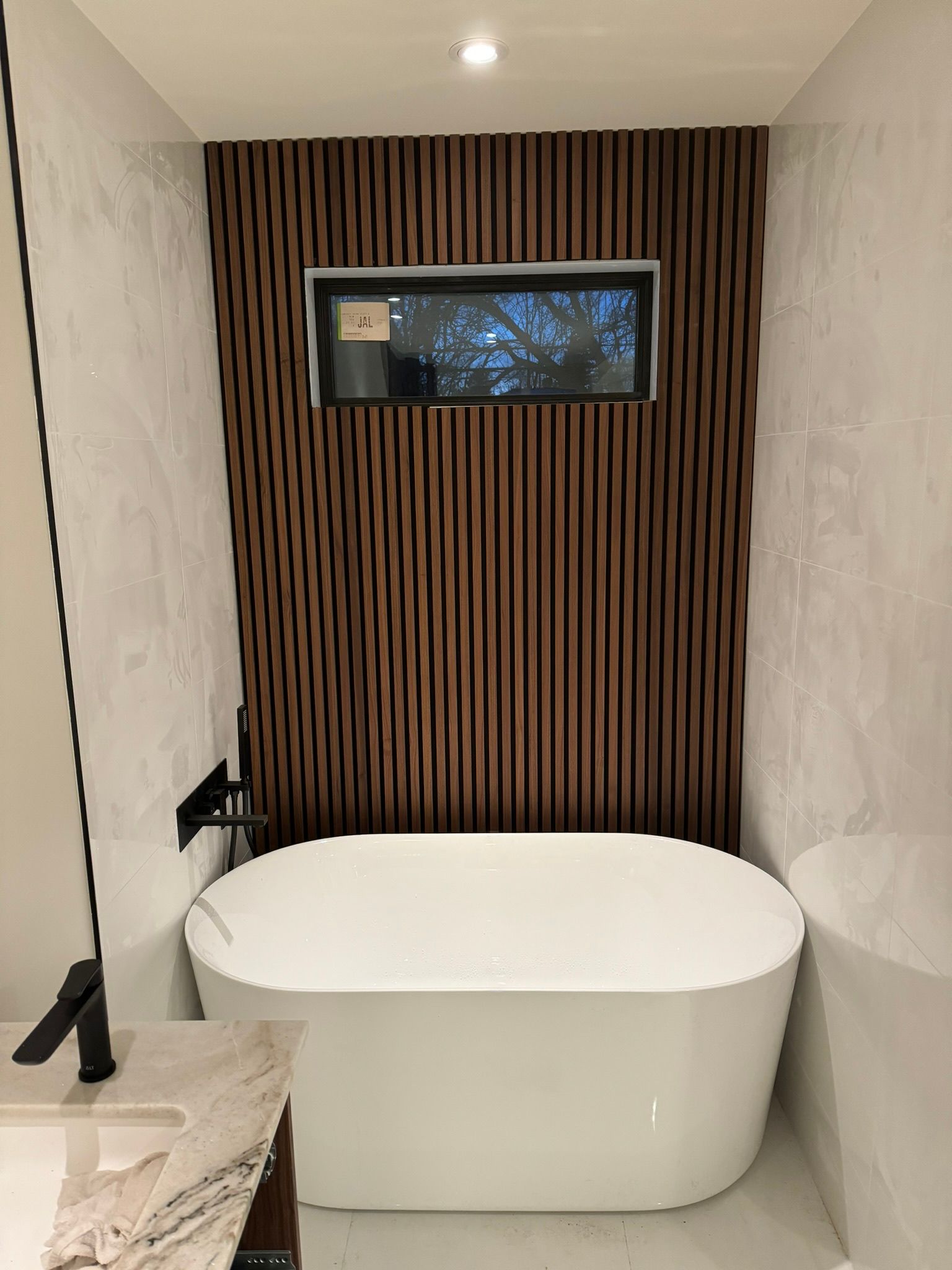 Salle de bains avec baignoire ovale blanche, mur lambrissé de bois foncé et petite fenêtre.