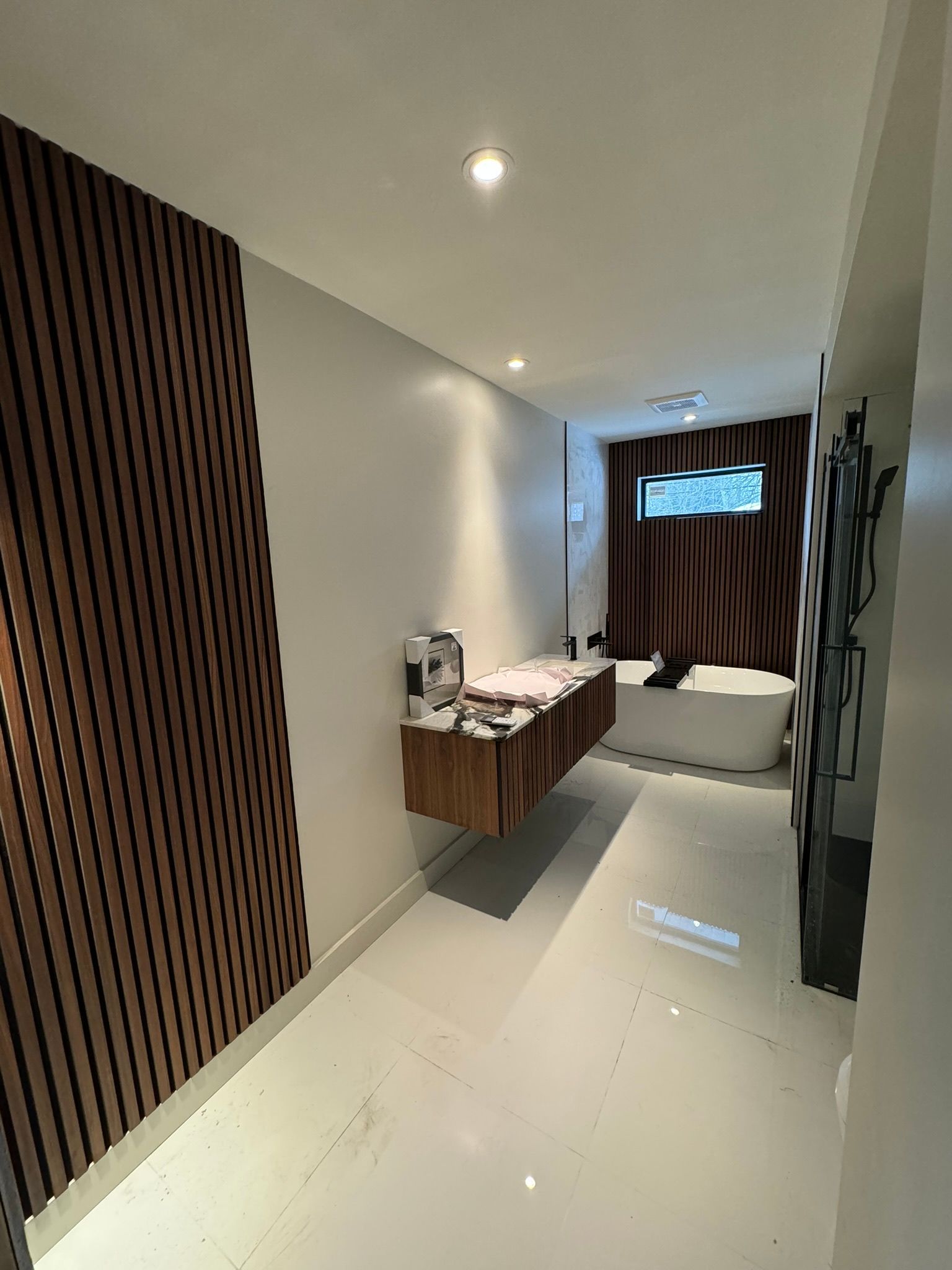 Couloir étroit avec mur lambrissé, armoire en bois suspendue, sol blanc et aperçu d'une salle de bains.