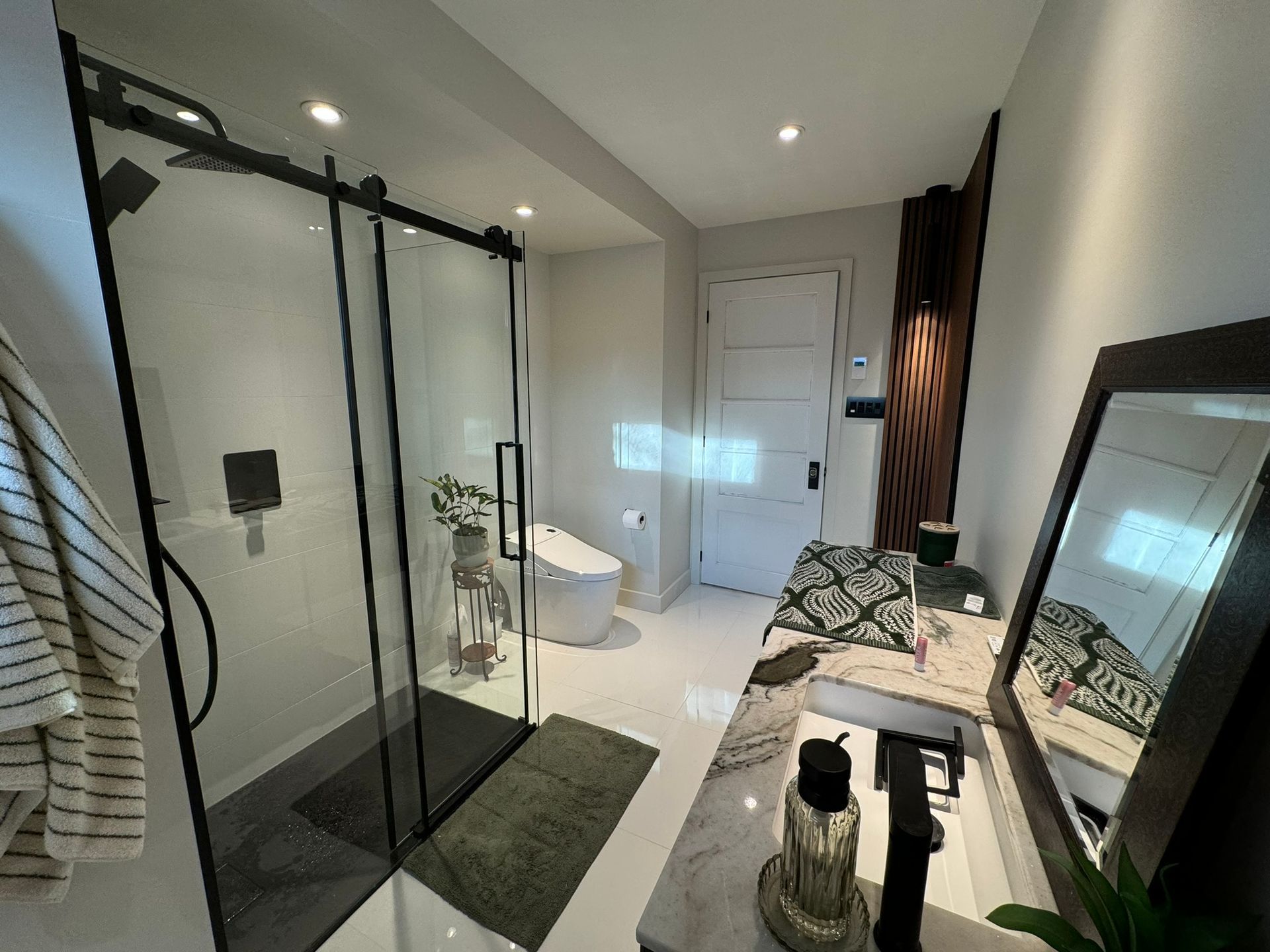 Salle de bains moderne avec douche en verre, toilettes, meuble-lavabo et serviette rayée.