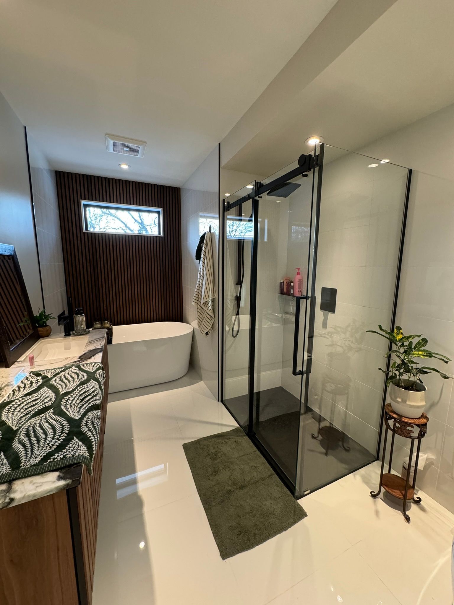 Salle de bains moderne avec douche en verre, baignoire îlot et meuble-lavabo en bois.
