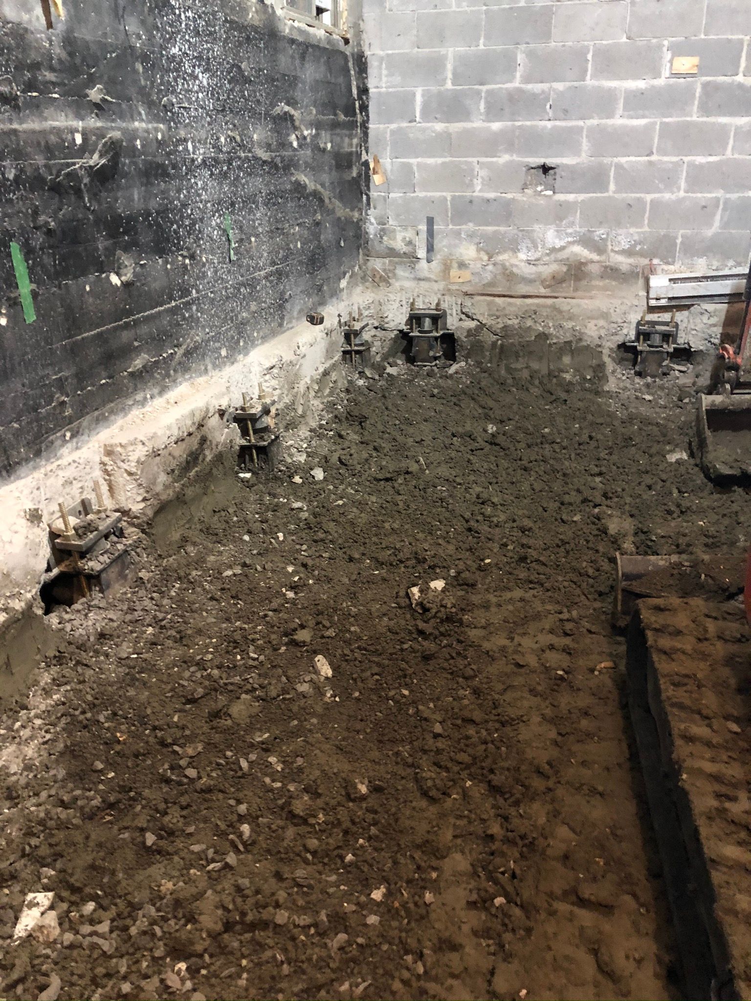 Chantier de construction avec sol en béton apparent et mur en parpaings, montrant la réparation des fondations avec des supports métalliques.