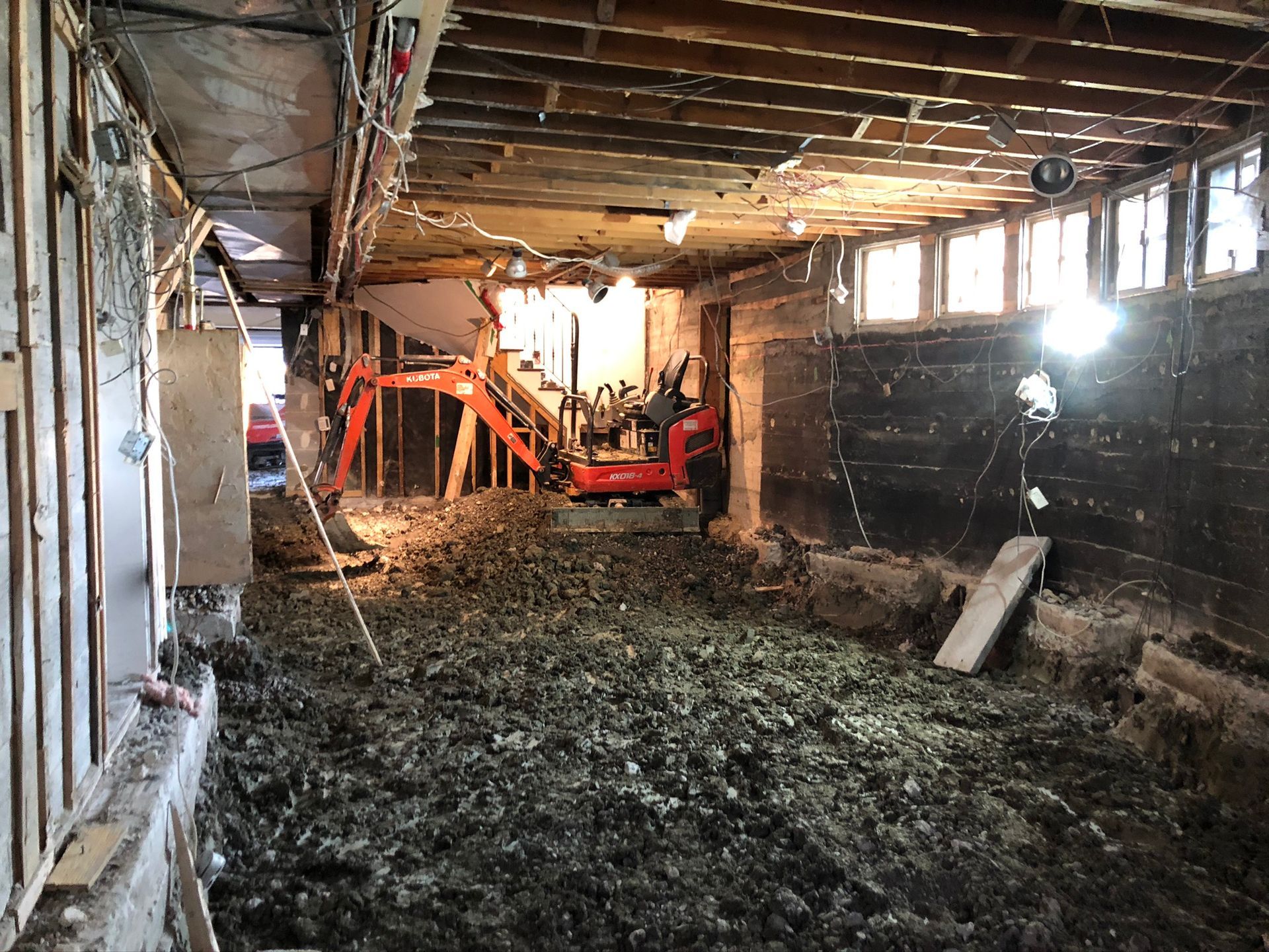 Chantier : Mini-pelle dans un sous-sol rempli de débris, murs apparents, éclairage zénithal.
