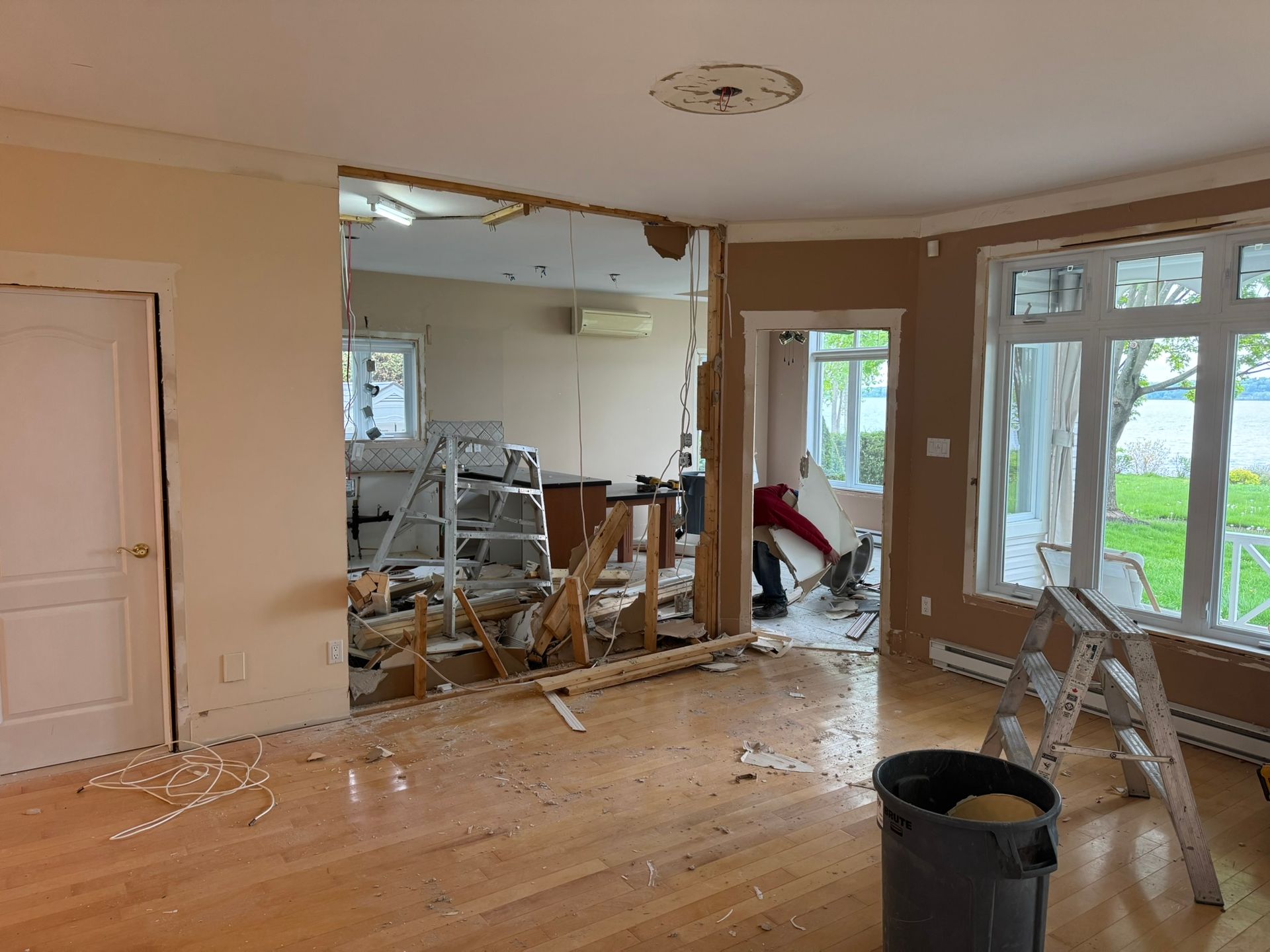 Rénovation intérieure ; démolition d'un mur en cours. Débris au sol. Personne utilisant une scie.