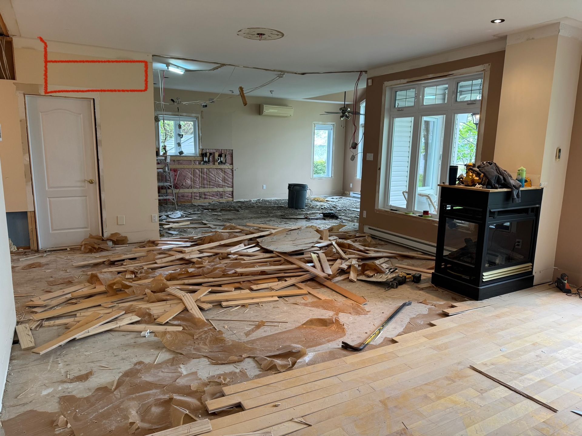 Pièce intérieure en rénovation, débris éparpillés au sol. La porte et la cheminée sont visibles.