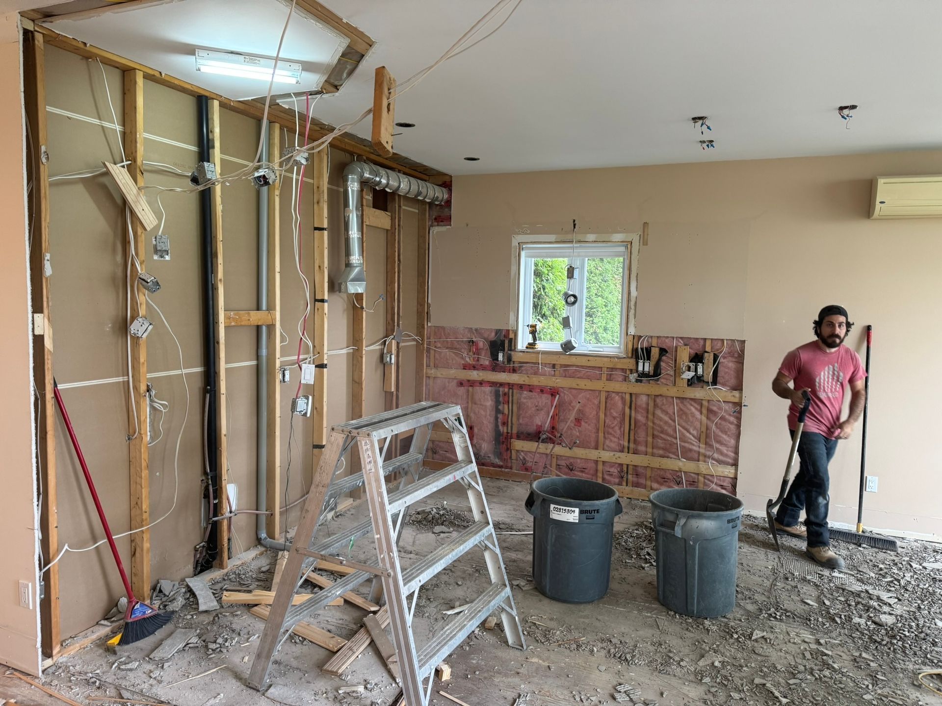 Rénovation de cuisine en cours : montants apparents, câbles électriques exposés, débris, ouvrier debout.