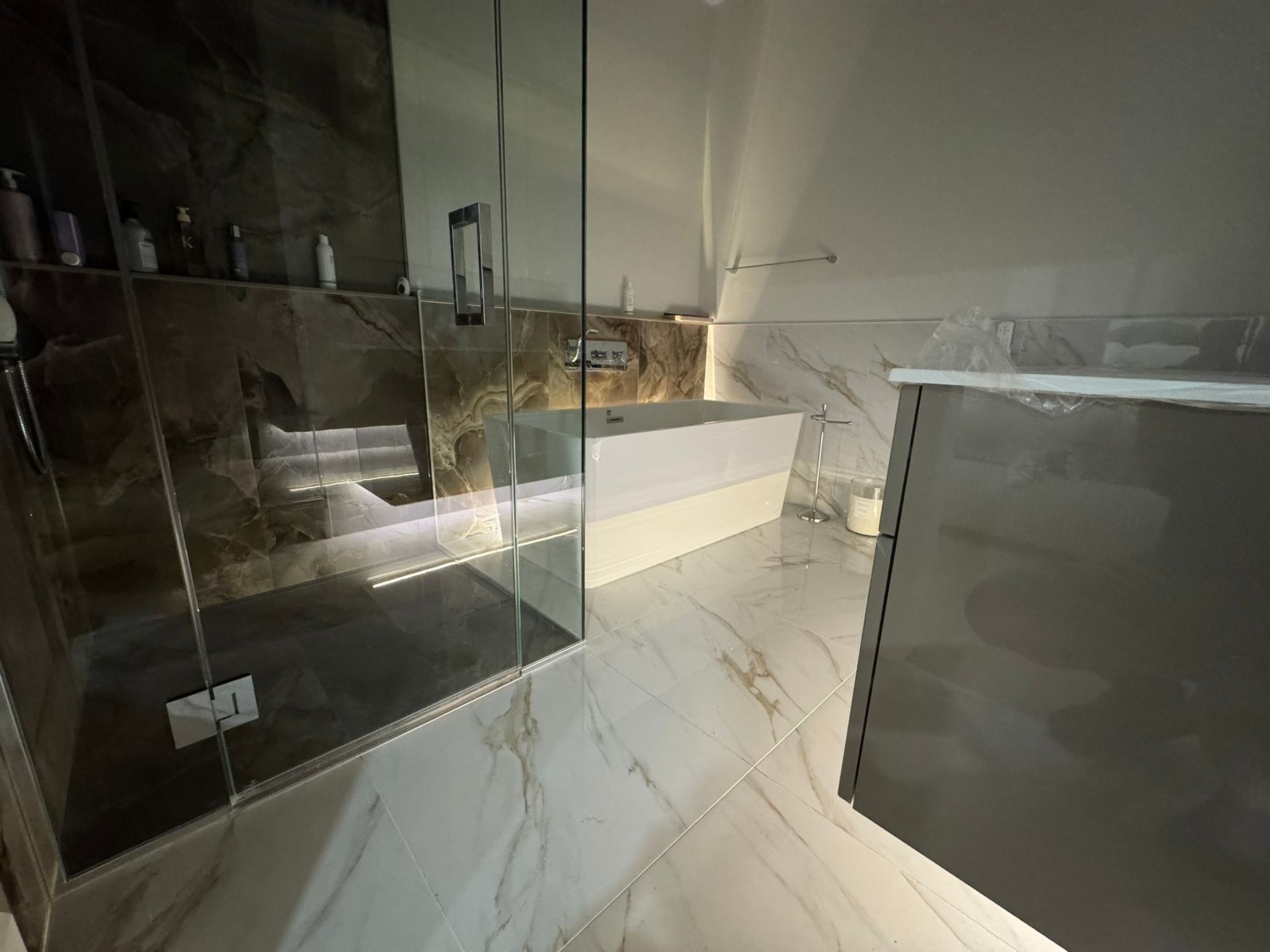 Salle de bains moderne avec douche en verre, baignoire et sol en carrelage de marbre.