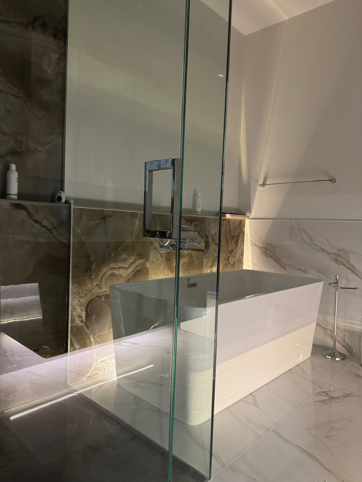 Salle de bains moderne avec baignoire rectangulaire blanche, paroi de douche en verre et carrelage en marbre.