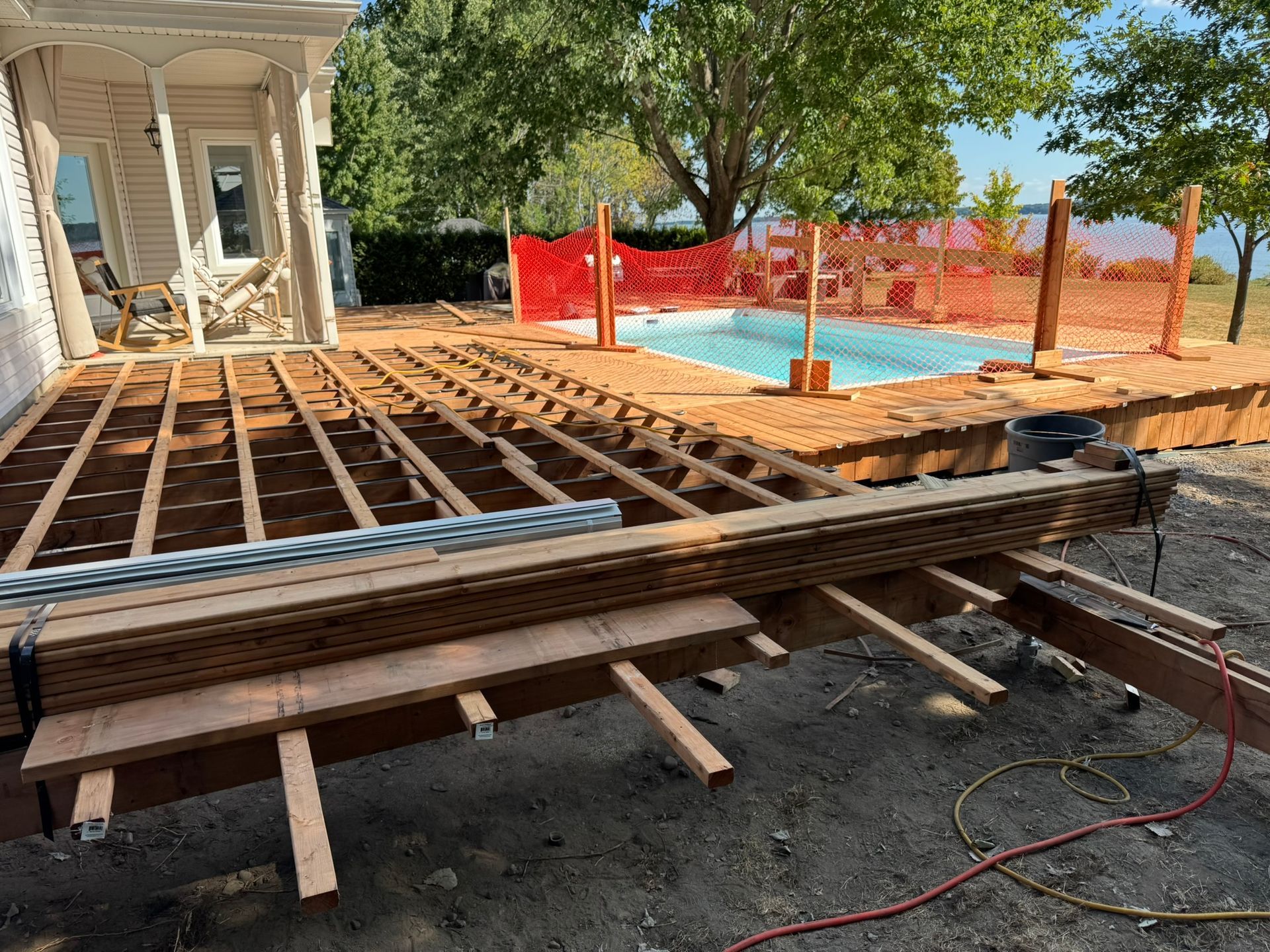 Terrasse en construction à côté d'une piscine. Charpente apparente, piles de bois, barrière de sécurité.