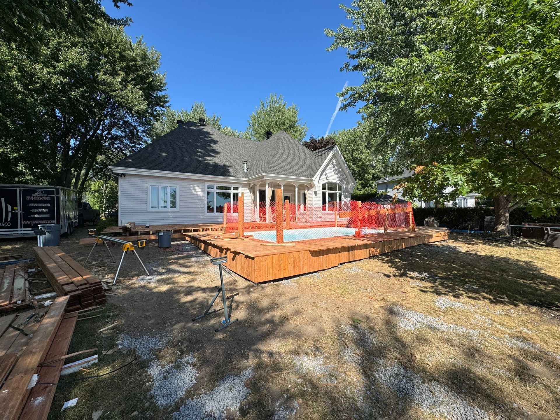 Maison avec une nouvelle terrasse en bois en construction dans un jardin bordé d'arbres