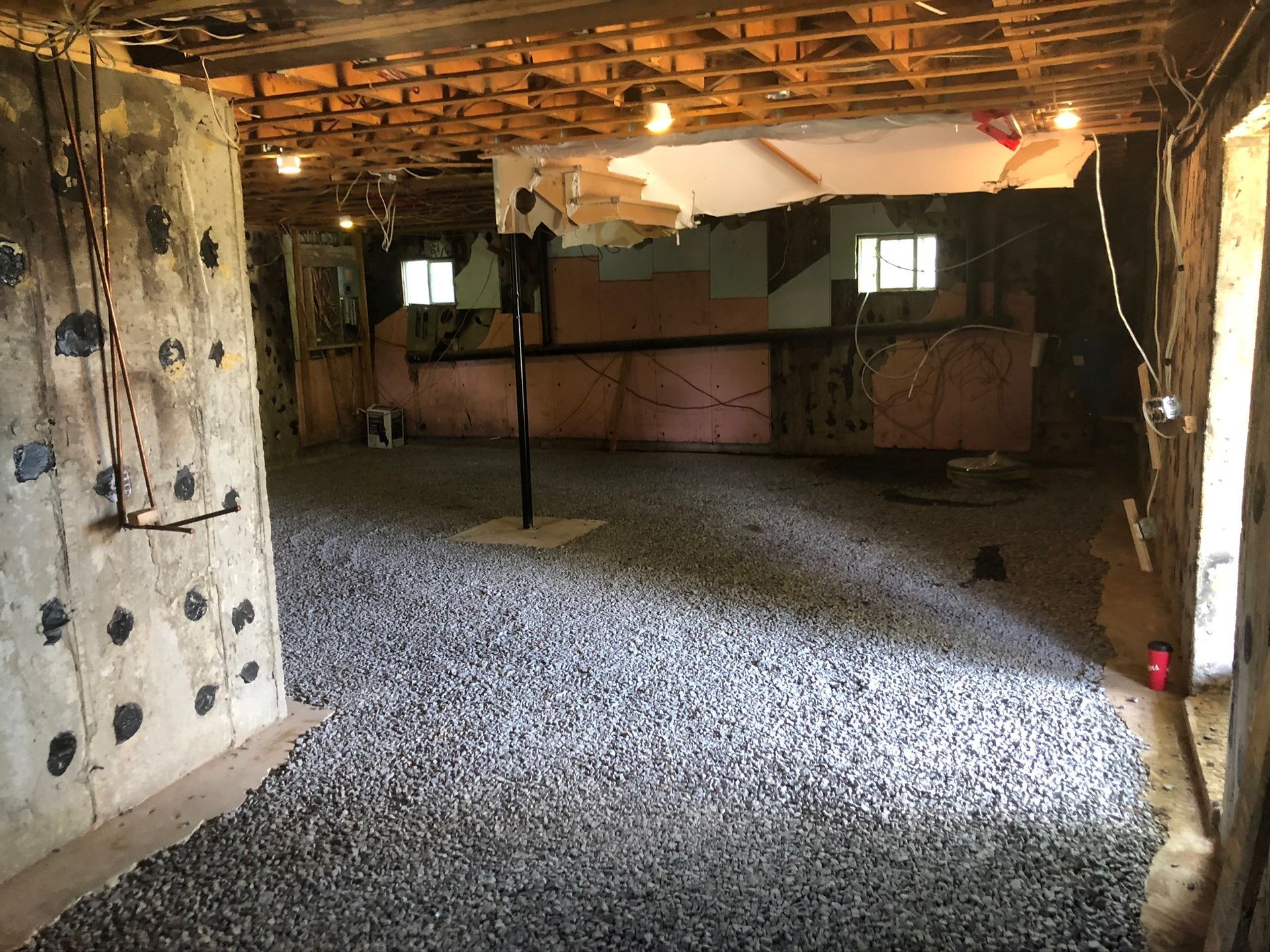 Pièce au sous-sol avec mur d'escalade, sol en gravier, poutres apparentes et coin bar non aménagé.