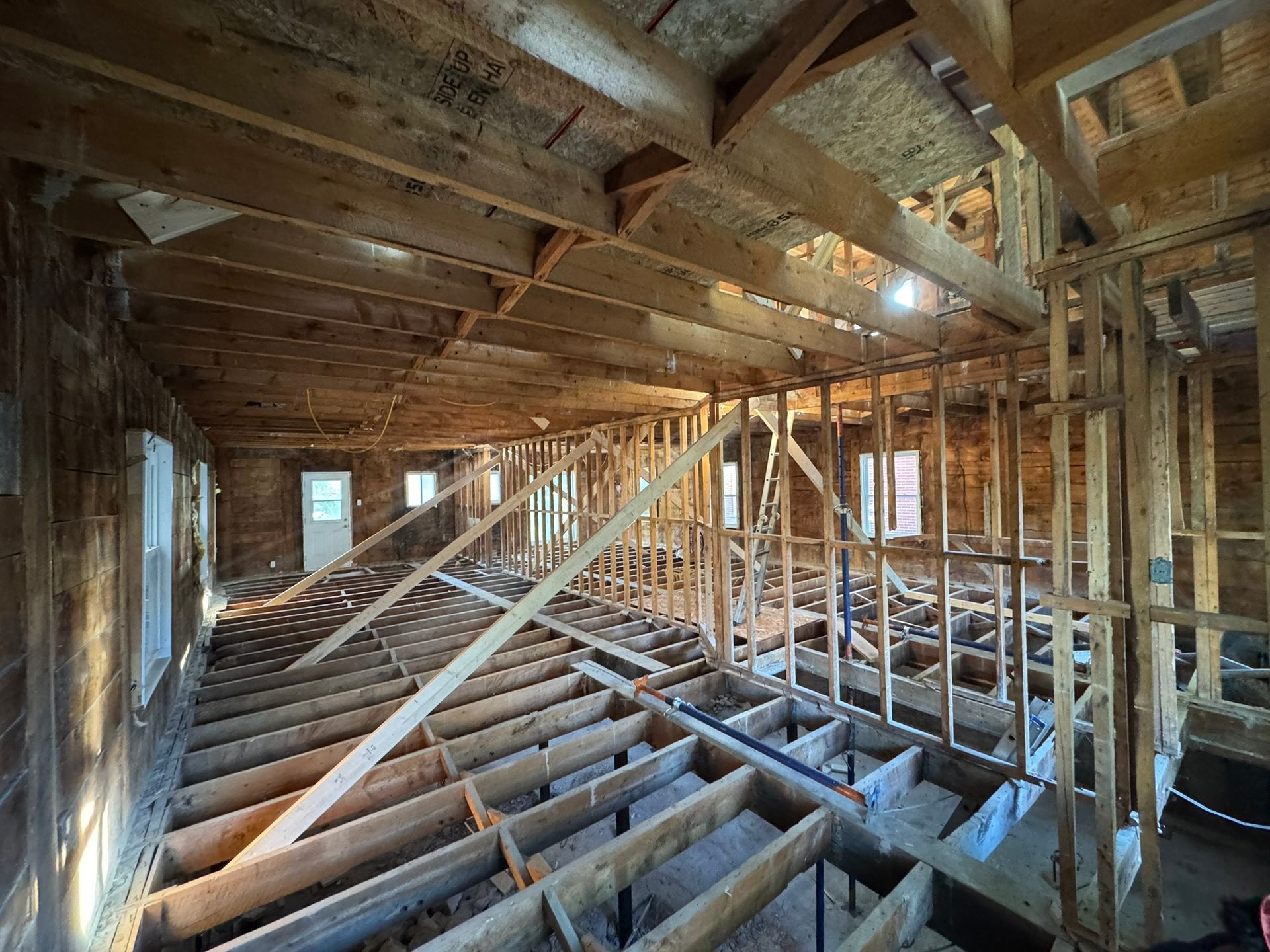Intérieur d'un bâtiment en rénovation, montrant les poutres, les montants et les solives en bois apparents.