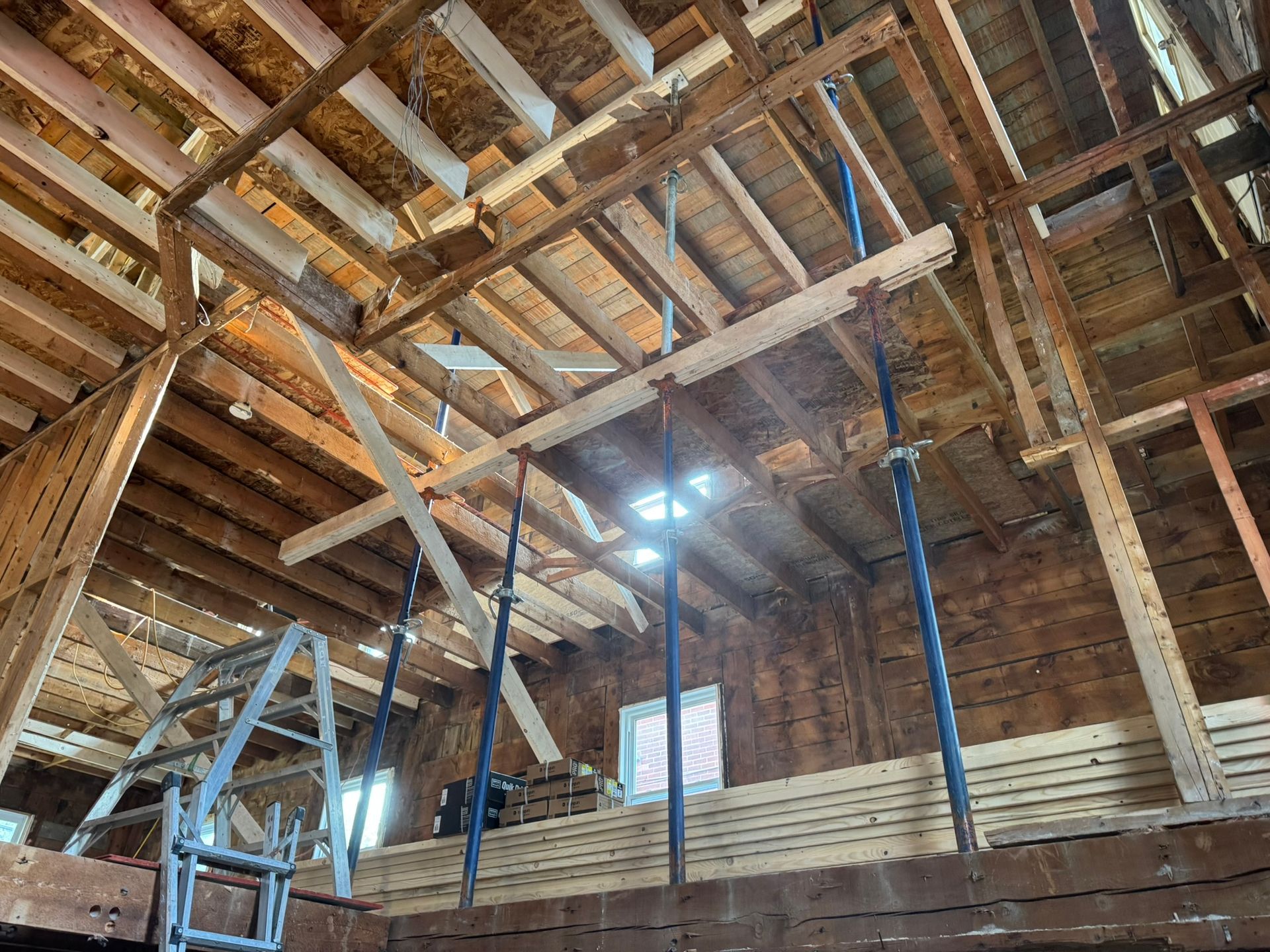 Vue intérieure d'un bâtiment en rénovation, avec des échafaudages soutenant les poutres du plafond.