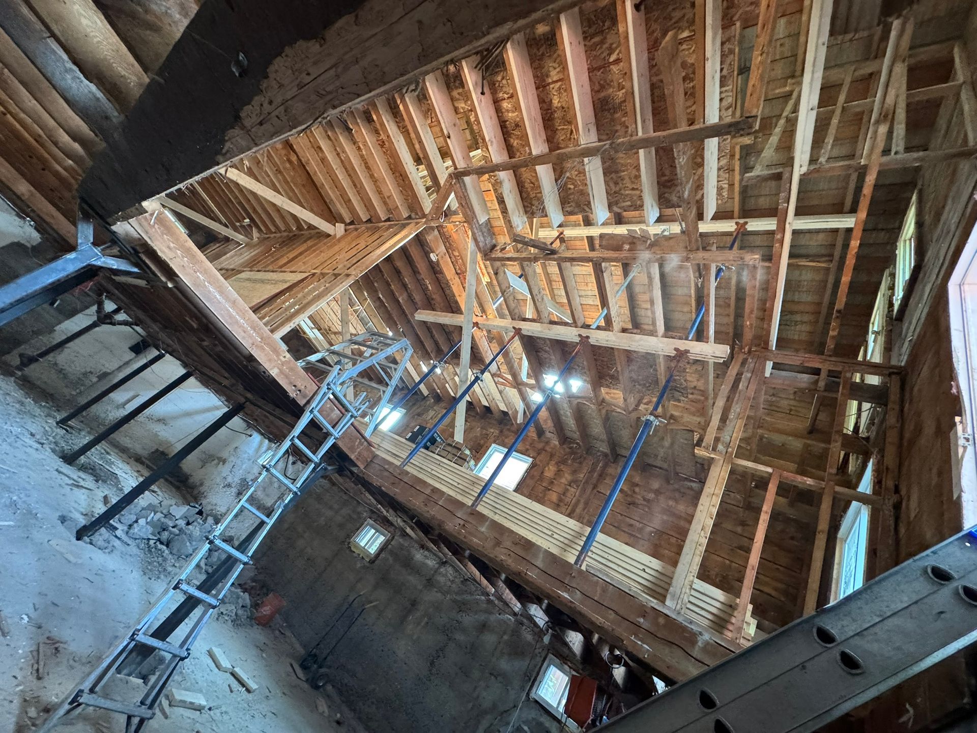 Vue intérieure d'un bâtiment en rénovation, montrant des poutres en bois apparentes et une échelle.