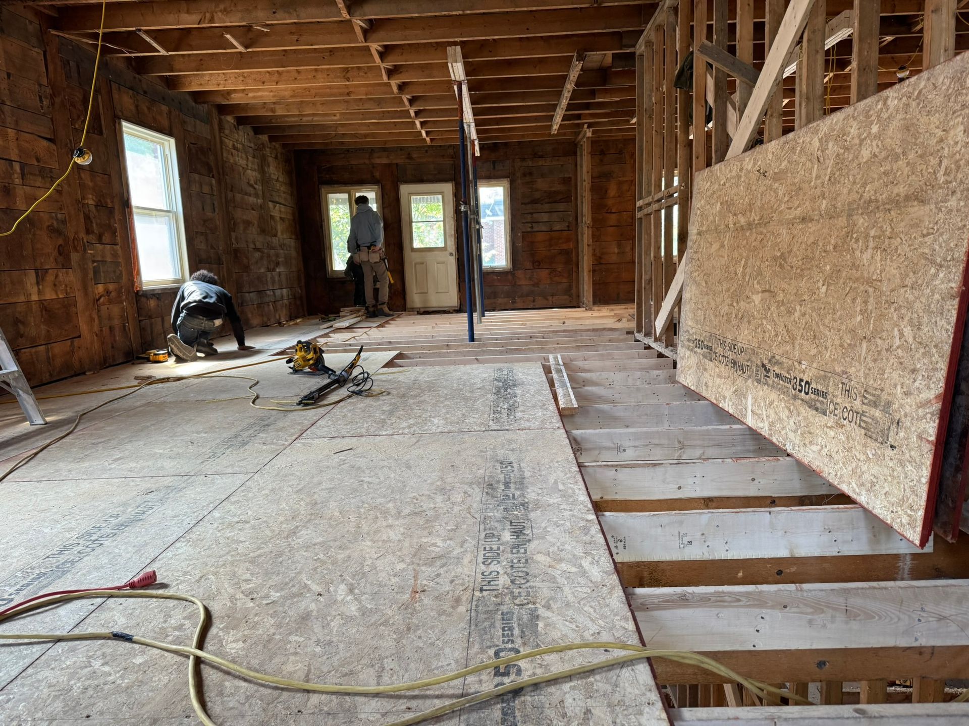 Intérieur d'une pièce en construction avec charpente apparente et ouvriers.