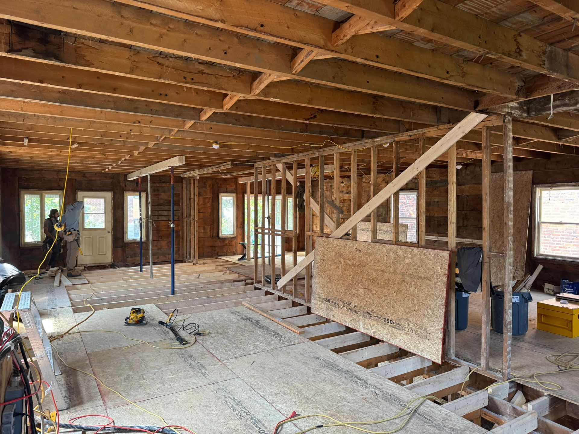Rénovation intérieure : murs et plafond ouverts, charpente apparente. Outils et matériaux de construction éparpillés.