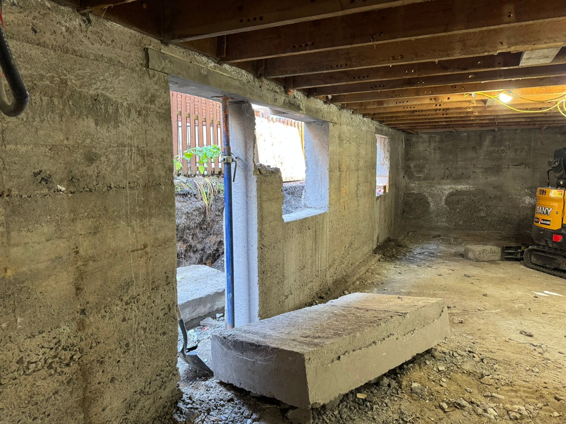 Intérieur d'une pièce en béton aux murs bruts. On distingue une porte, deux fenêtres et des poutres apparentes au plafond.