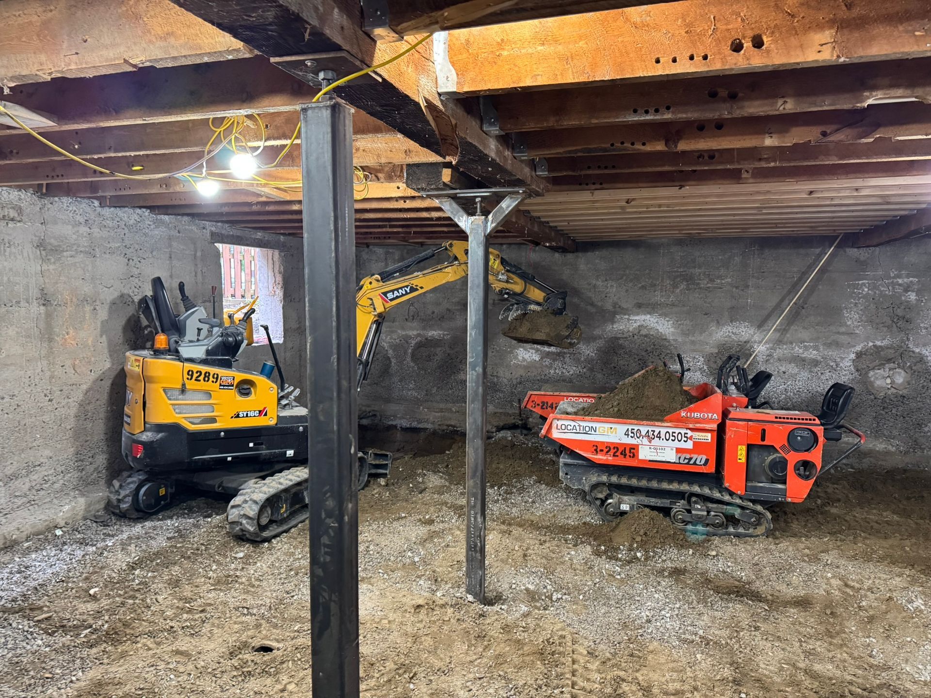 Engins de chantier en activité dans un sous-sol : excavatrices, poutres de soutien en acier, terre, murs en béton.
