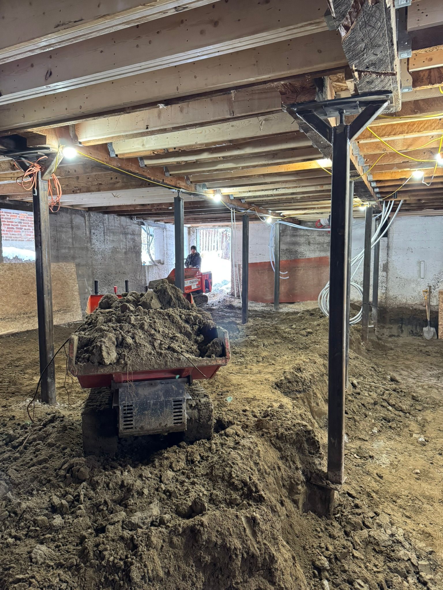 Sous-sol intérieur avec sol en terre battue. Un petit véhicule transporte la terre. Des poutres de soutien en acier soutiennent le plafond en bois.