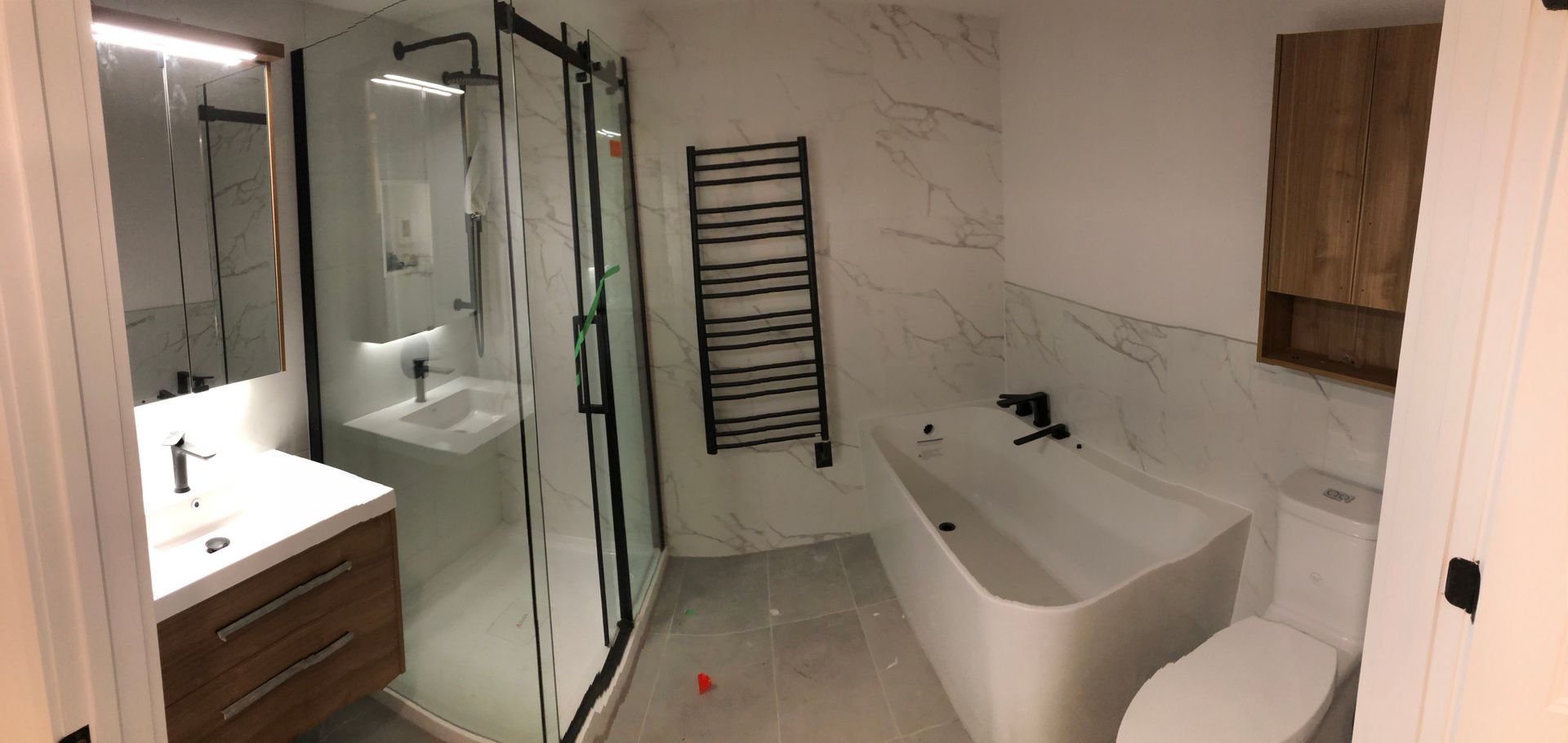 Salle de bains moderne avec murs en marbre, douche à cadre noir, baignoire îlot et meuble-lavabo en bois.