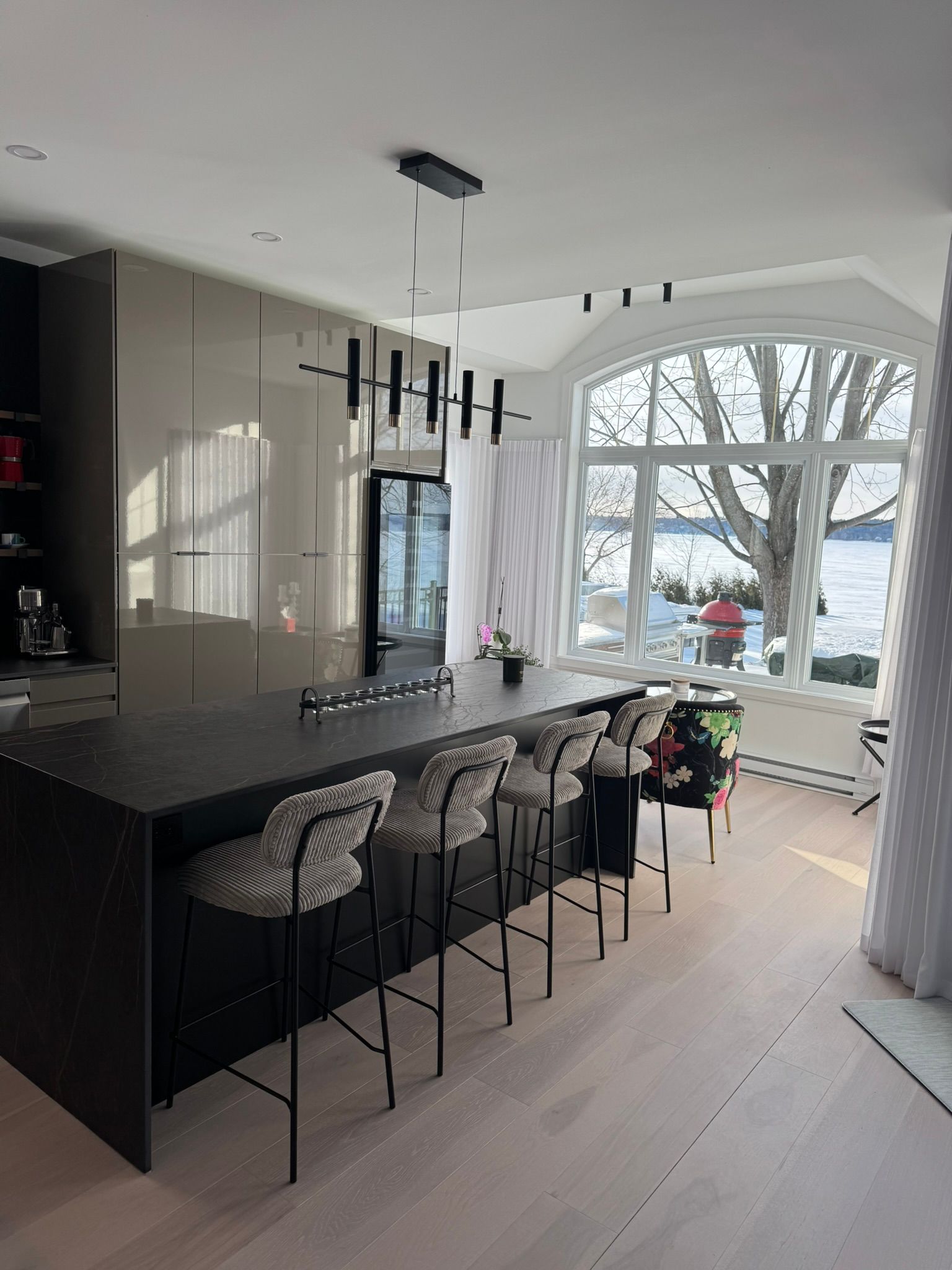 Cuisine moderne avec îlot central, tabourets de bar et grande fenêtre donnant sur l'eau.