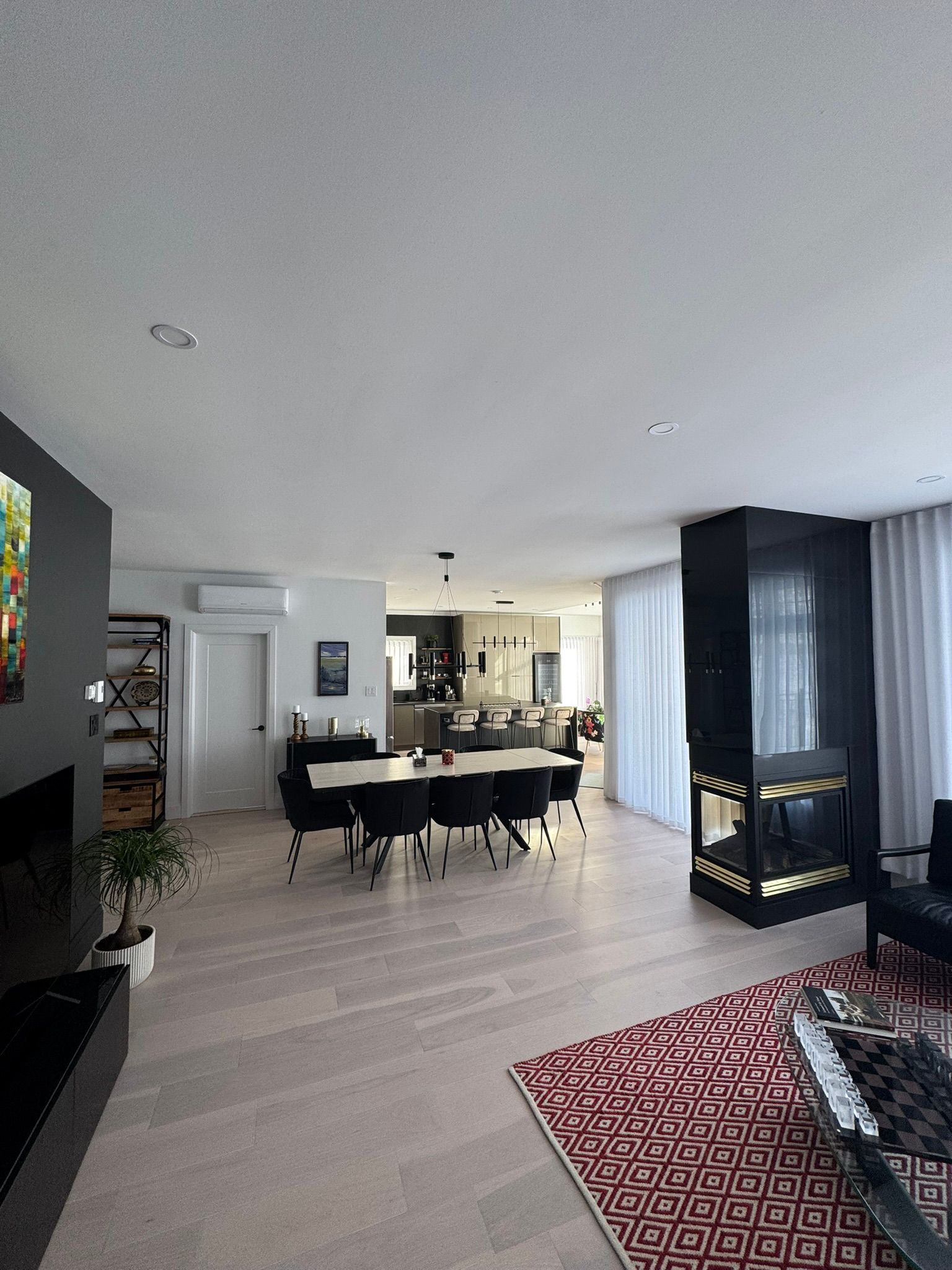 Salon moderne et spacieux avec coin repas, cheminée et parquet clair. Décoration en noir et blanc rehaussée d'un tapis rouge.