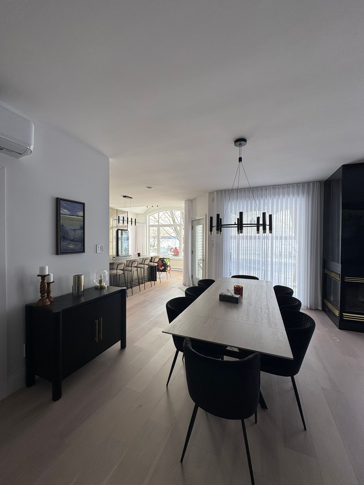 Salle à manger moderne avec une longue table, des chaises noires et un buffet noir.