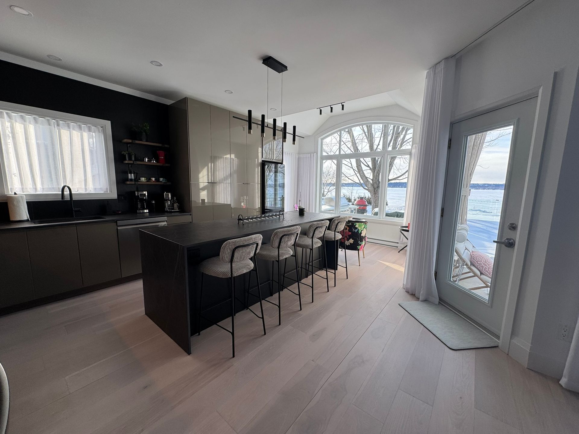 Cuisine moderne avec îlot central, comptoirs noirs et vue sur le front de mer grâce à une grande baie vitrée cintrée.