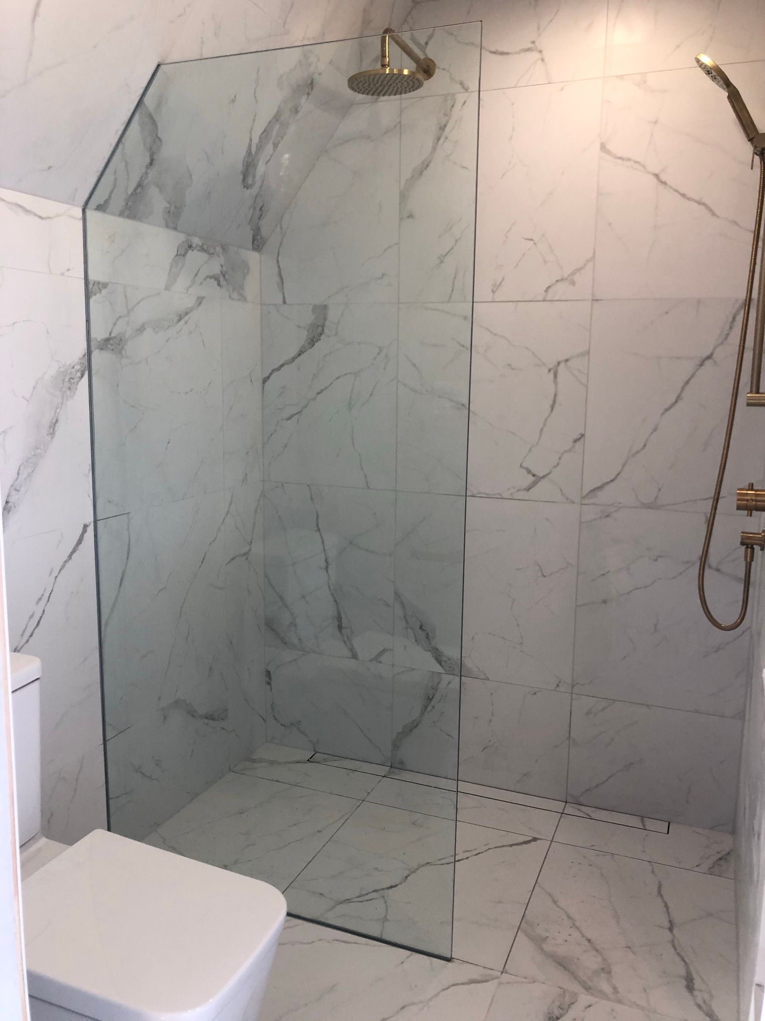 Cabine de douche avec carrelage à motif marbre et paroi en verre ; robinetterie dorée.