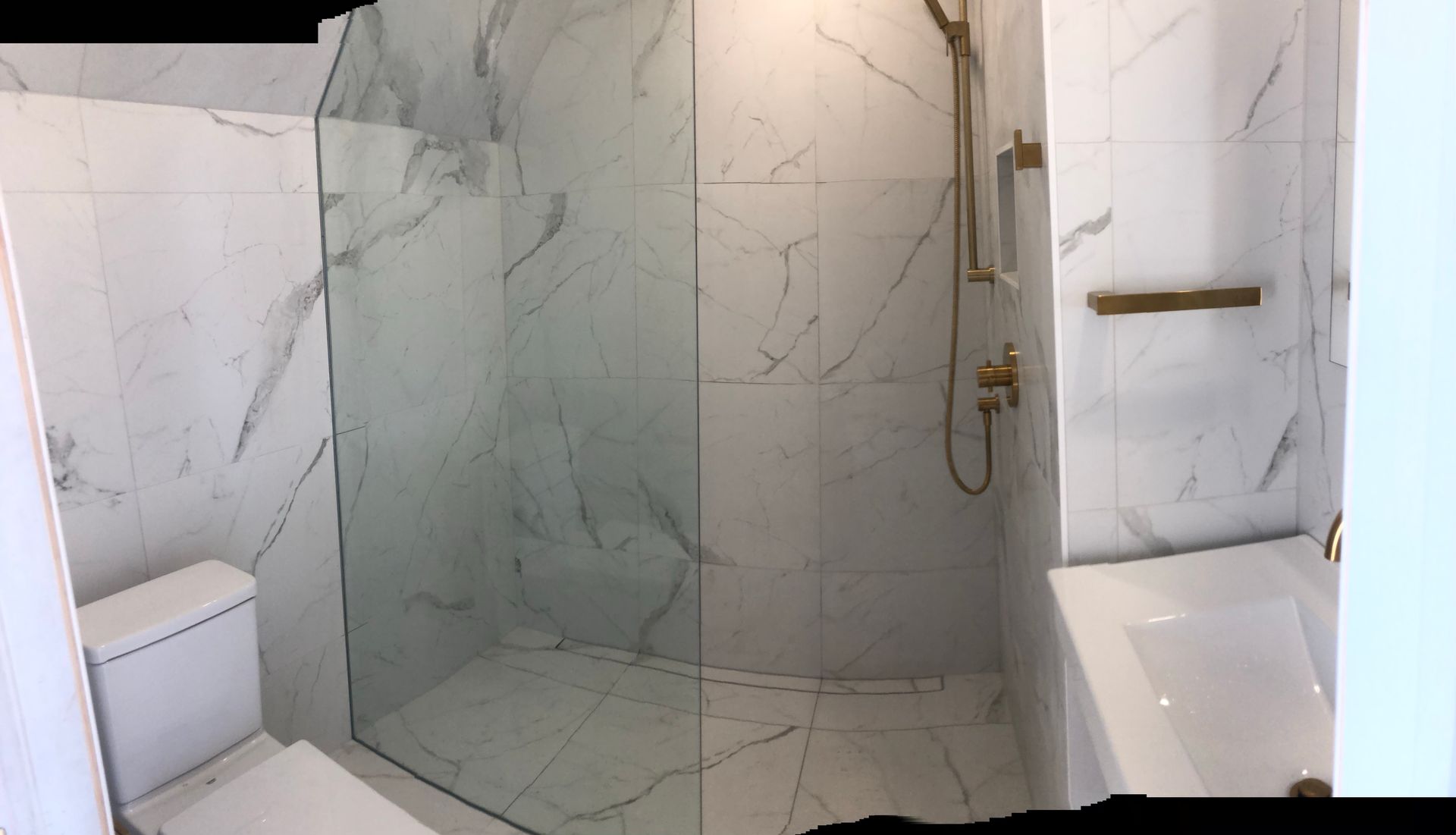 Une salle de bains moderne avec des carreaux imitation marbre blanc, une cabine de douche en verre et des accessoires dorés.