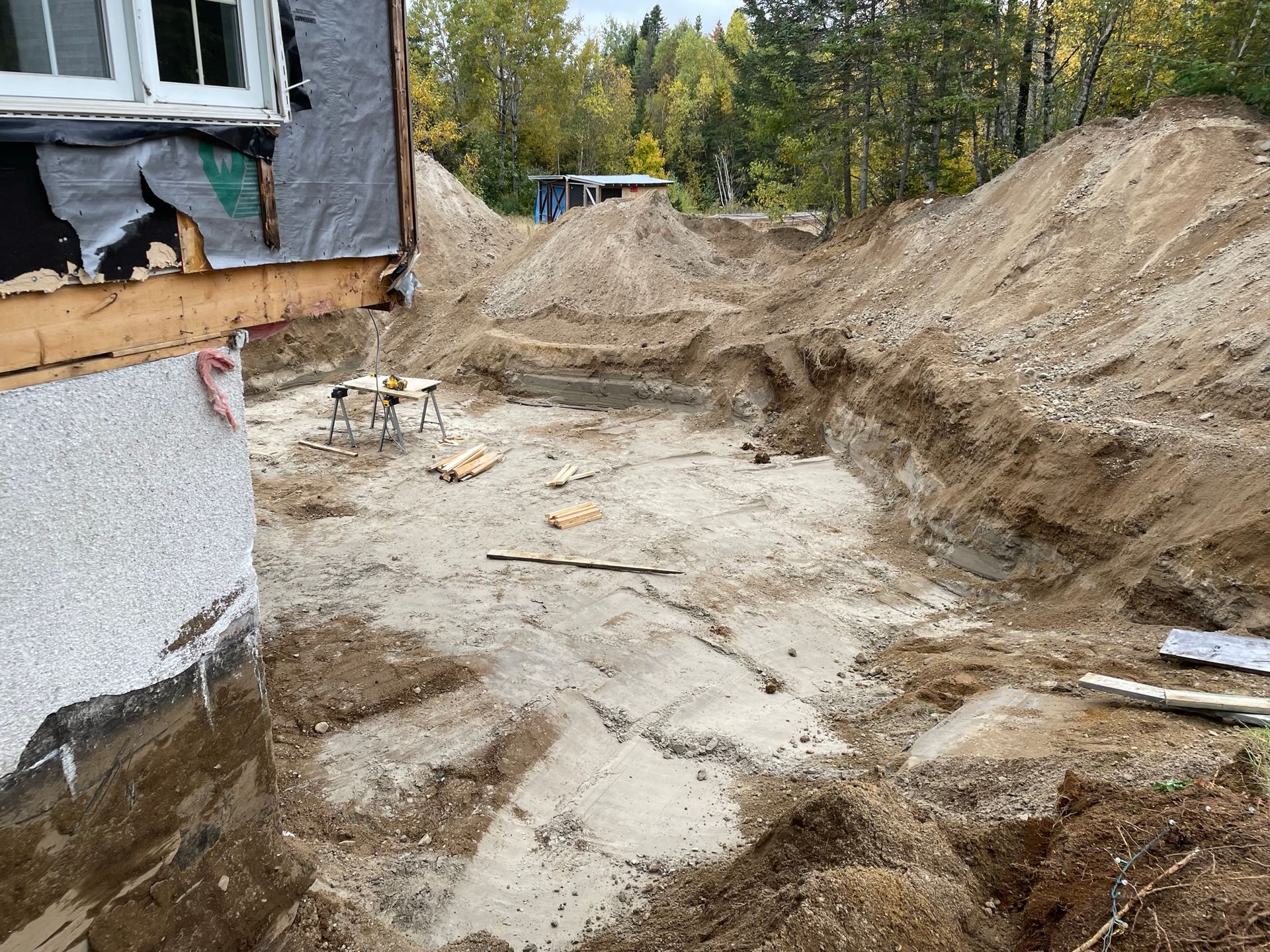 Chantier de construction avec une profonde excavation, des tas de terre et une partie d'une maison.