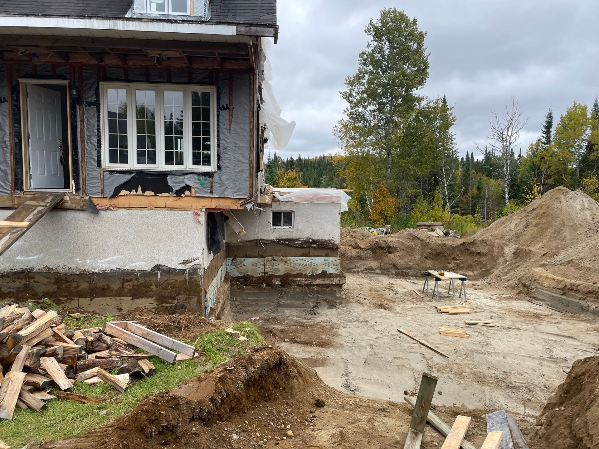 Maison en rénovation, fondations apparentes et travaux de terrassement en cours. Vue extérieure par temps nuageux.