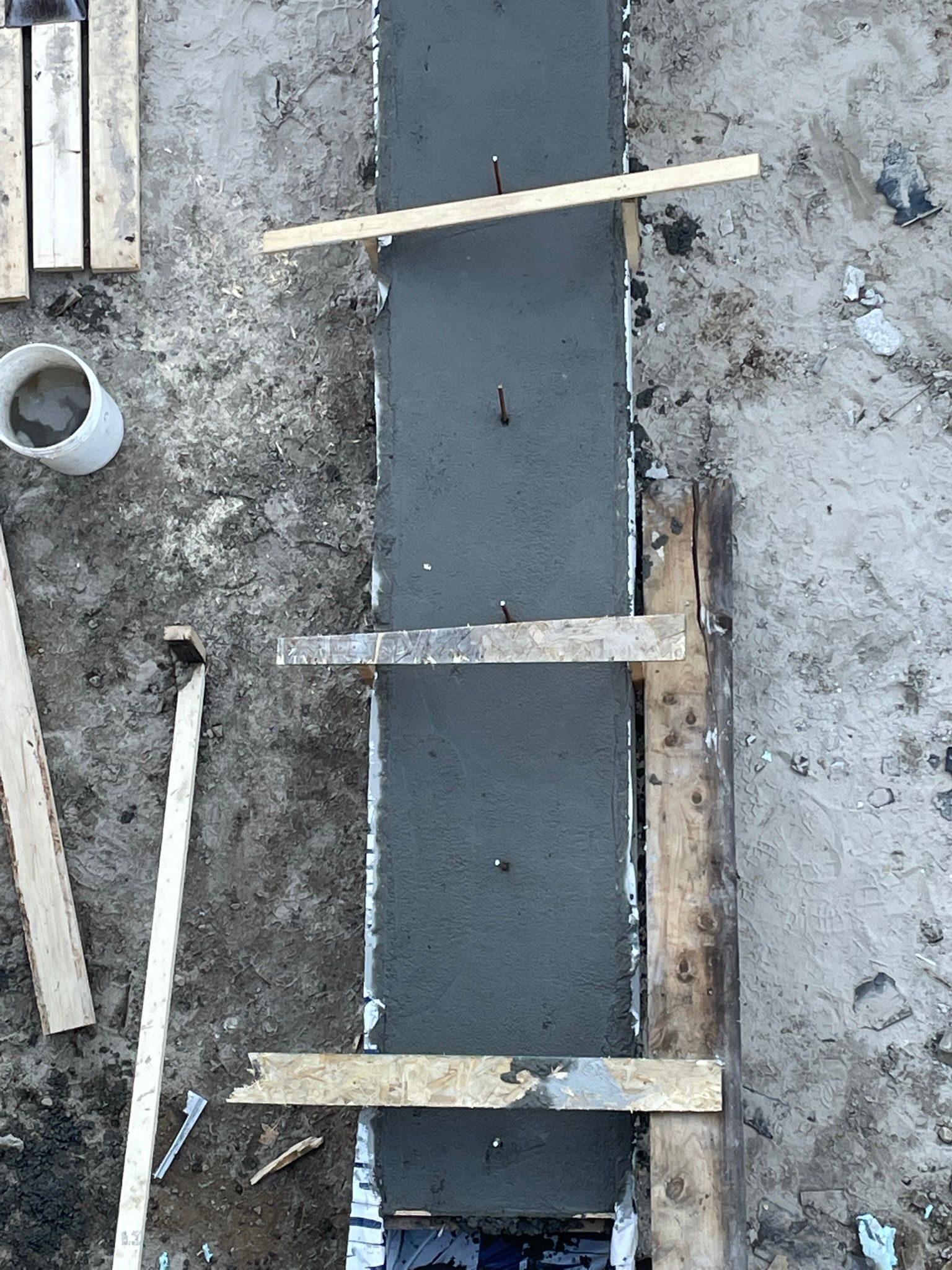 Du béton est coulé dans une armature en bois, fixée par des supports, à l'extérieur.