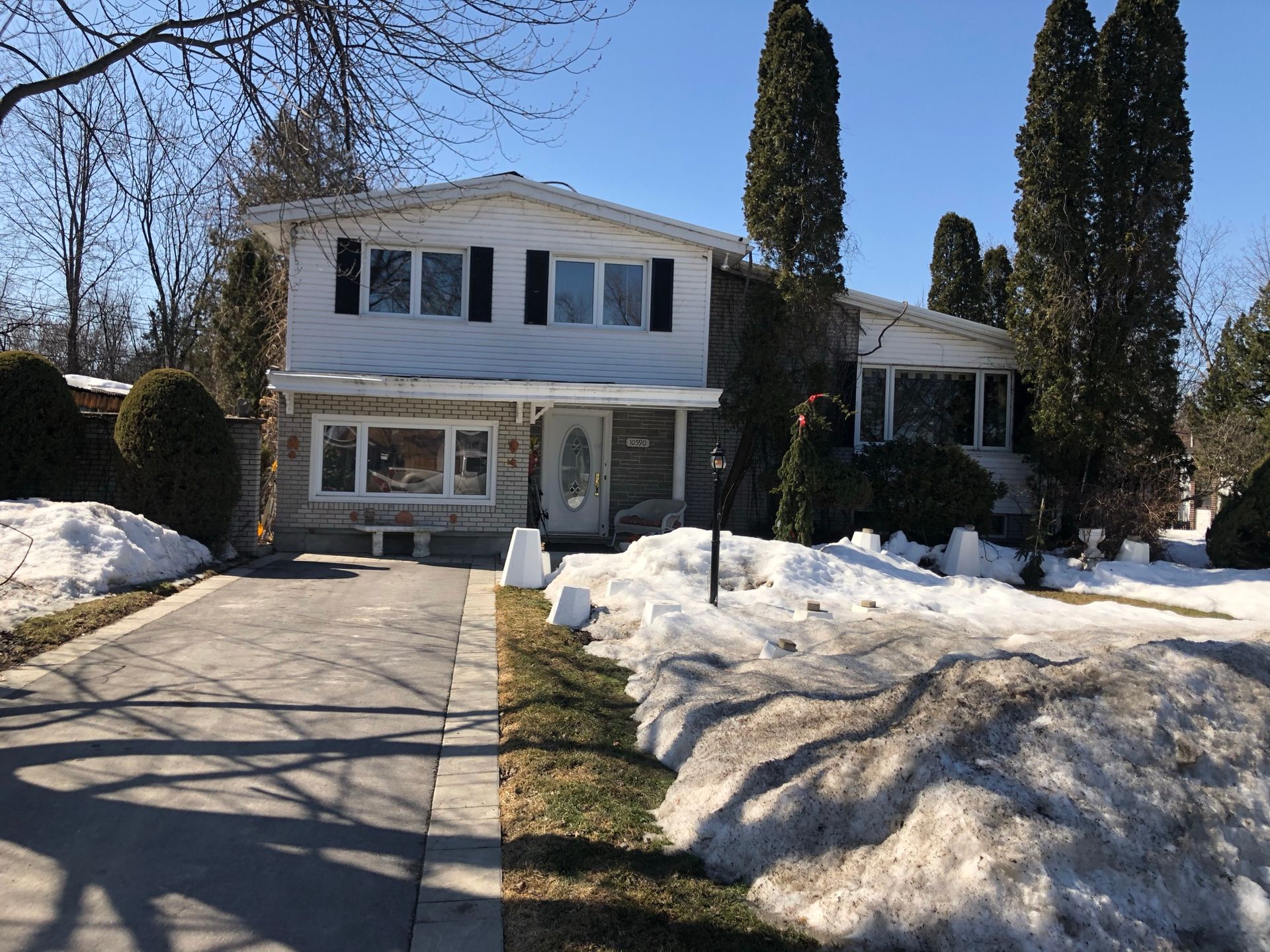 Maison avec une longue allée, de la neige au sol et des conifères.