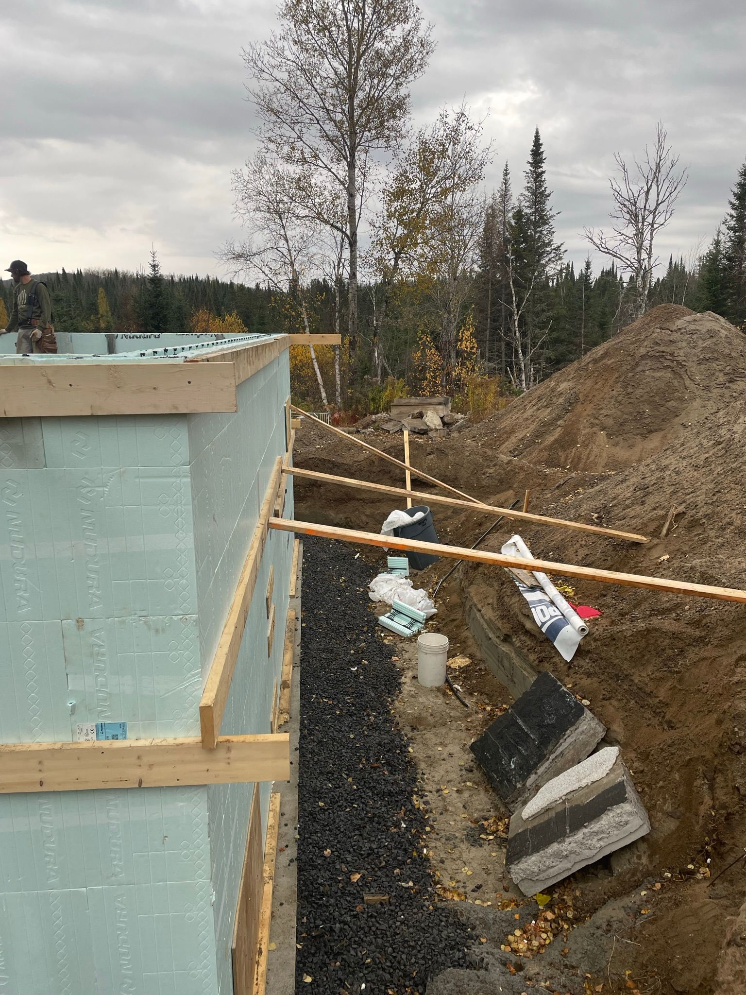 Chantier de construction avec mur en mousse bleue, tuyaux de drainage et terre.