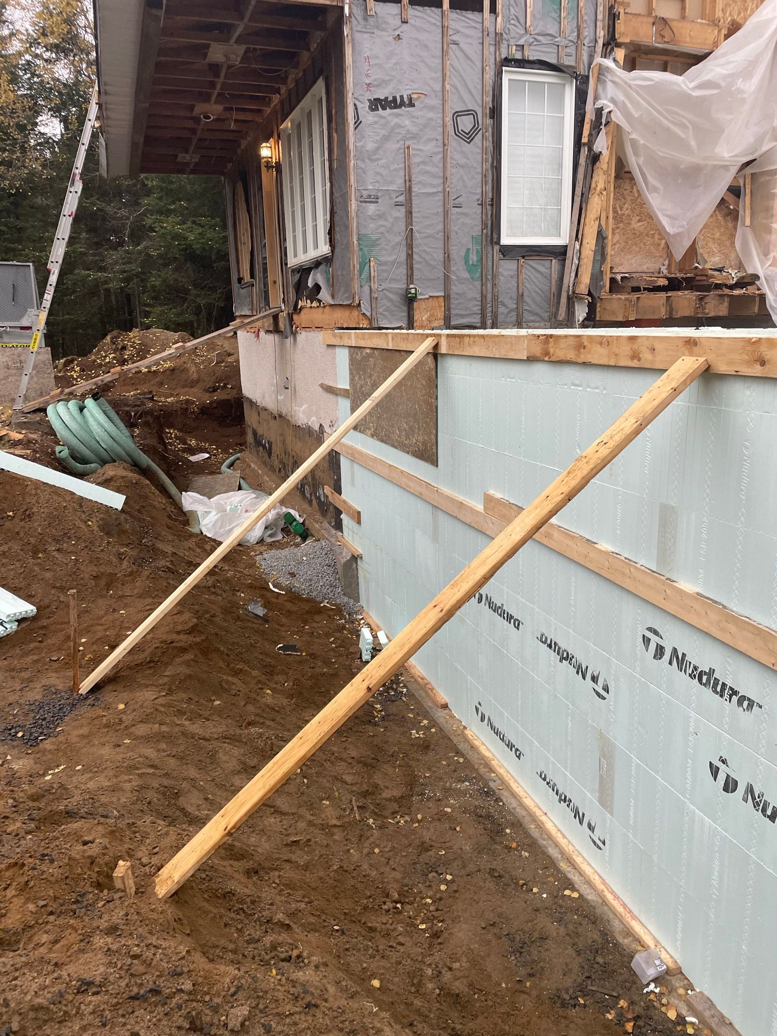 Chantier de construction : maison partiellement construite avec fondations et isolation apparentes, soutenue par des étais en bois.