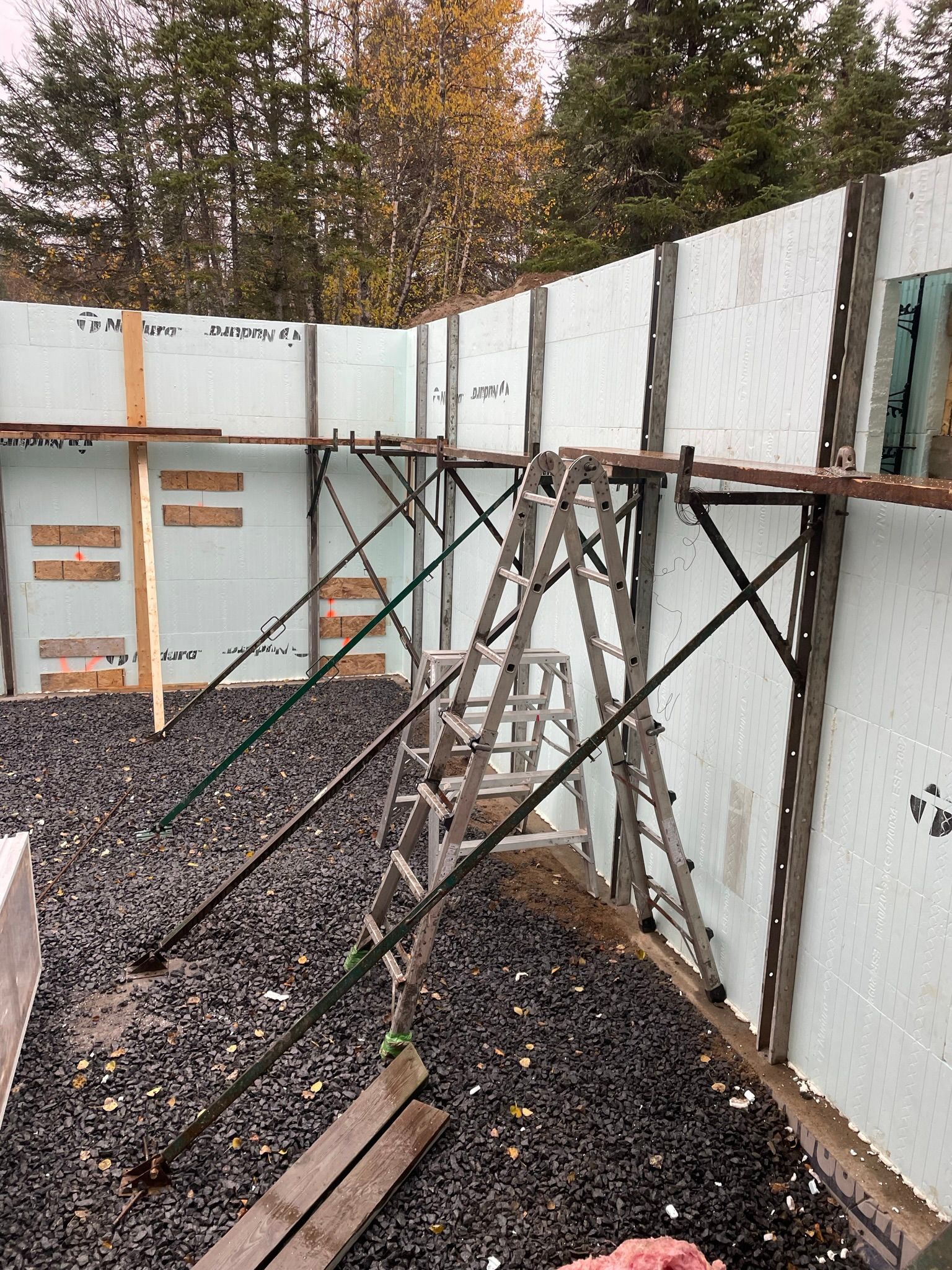 Chantier de construction avec coffrages en béton isolés, soutenus par des étais métalliques et une échelle.