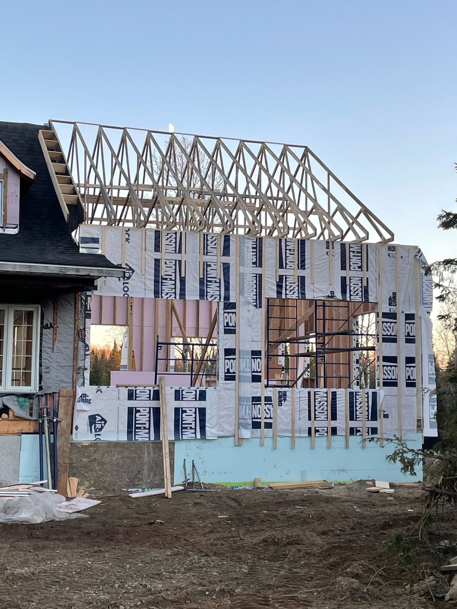 Construction d'une extension de maison ; ossature bois, isolation et charpente apparentes sur un ciel dégagé.