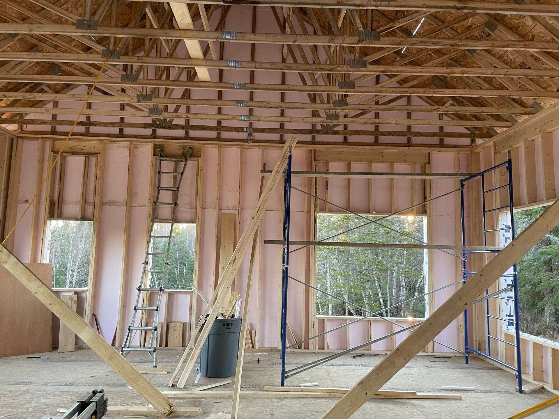 Intérieur d'un bâtiment en construction, montrant la charpente en bois, l'isolation et les fenêtres. Échafaudages visibles.