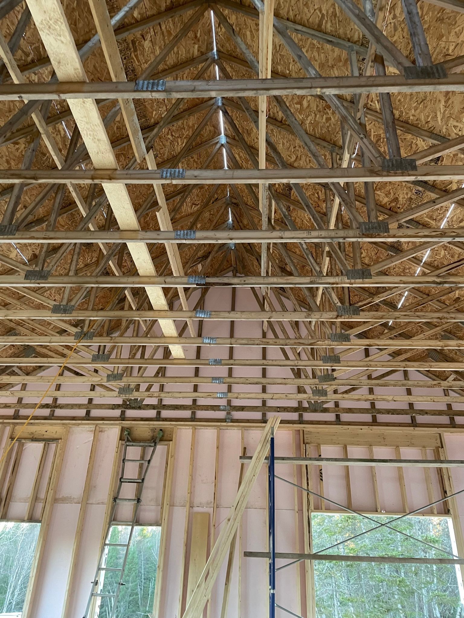 Vue intérieure d'un bâtiment en construction, montrant la charpente du toit en bois et l'isolation.