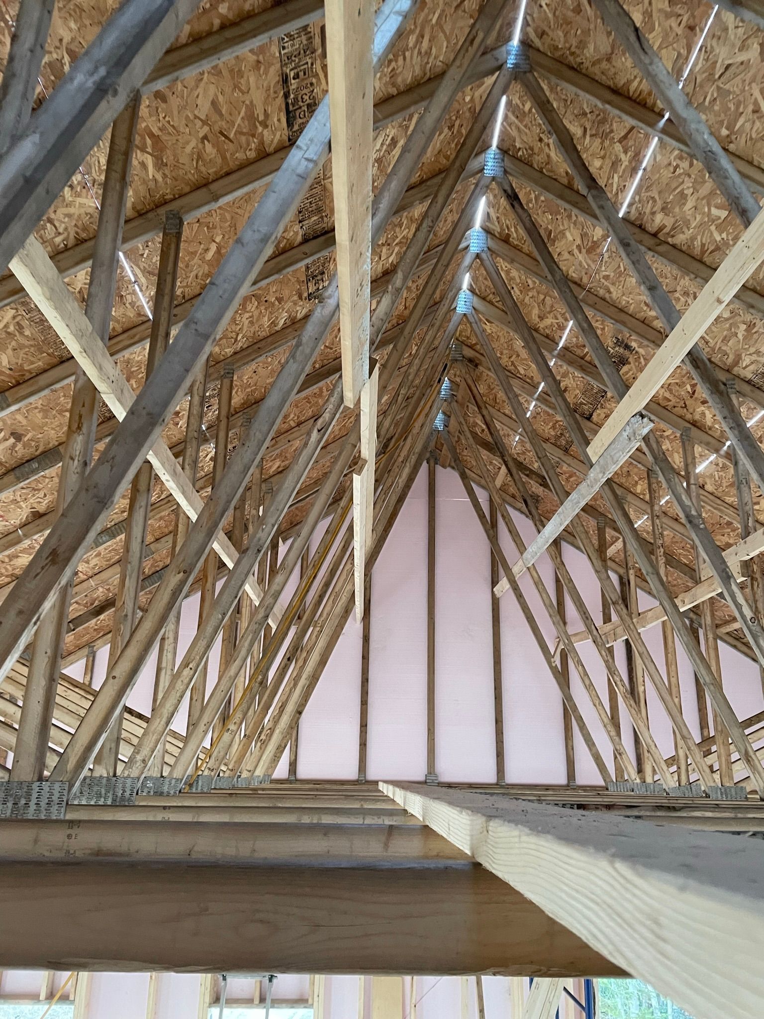 Vue intérieure d'une charpente de toit inachevée, avec chevrons et revêtement en bois.