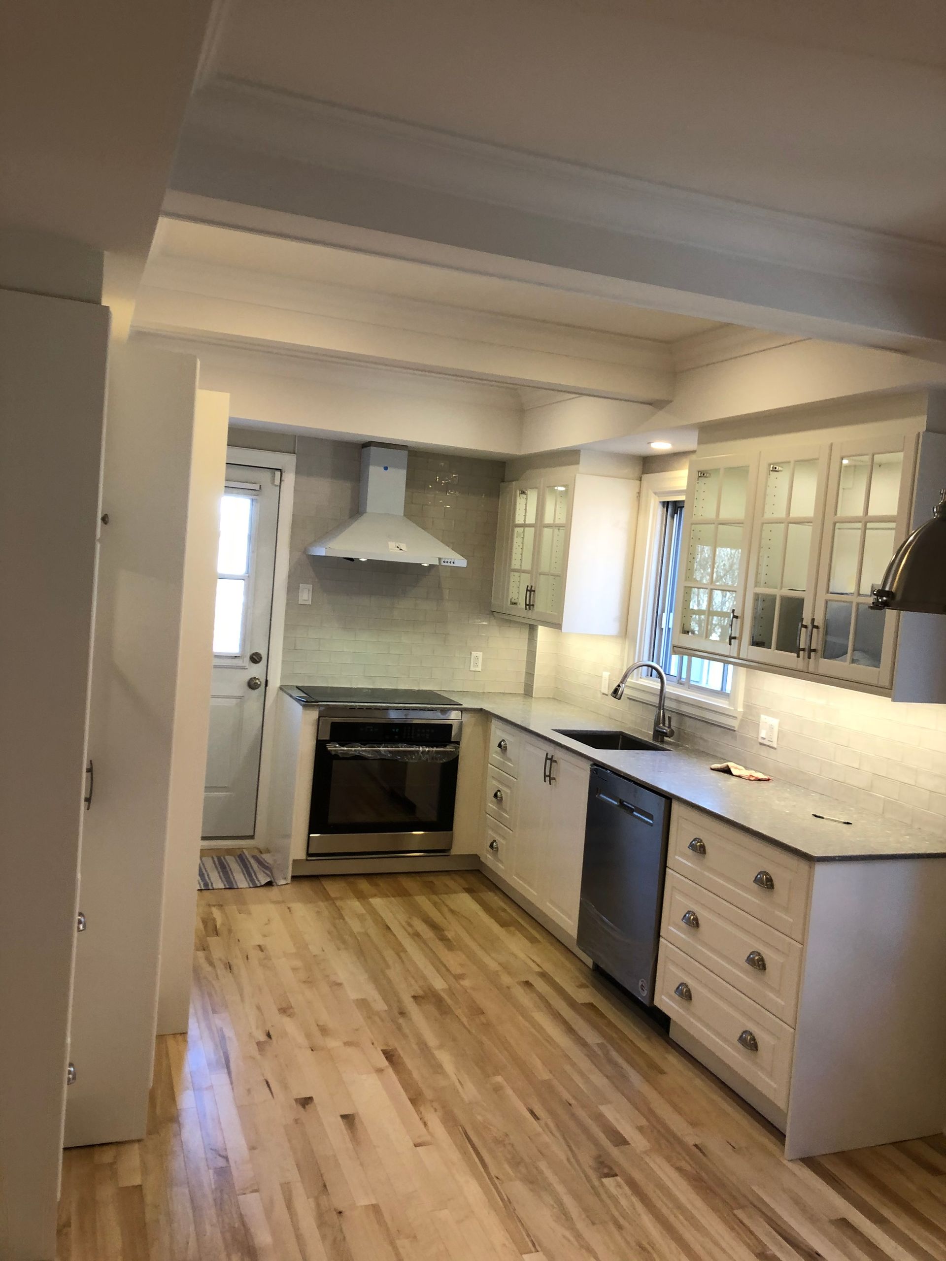 Rénovation lumineuse d'une cuisine : armoires blanches, électroménagers en acier inoxydable, plancher en bois clair et crédence en carrelage gris.
