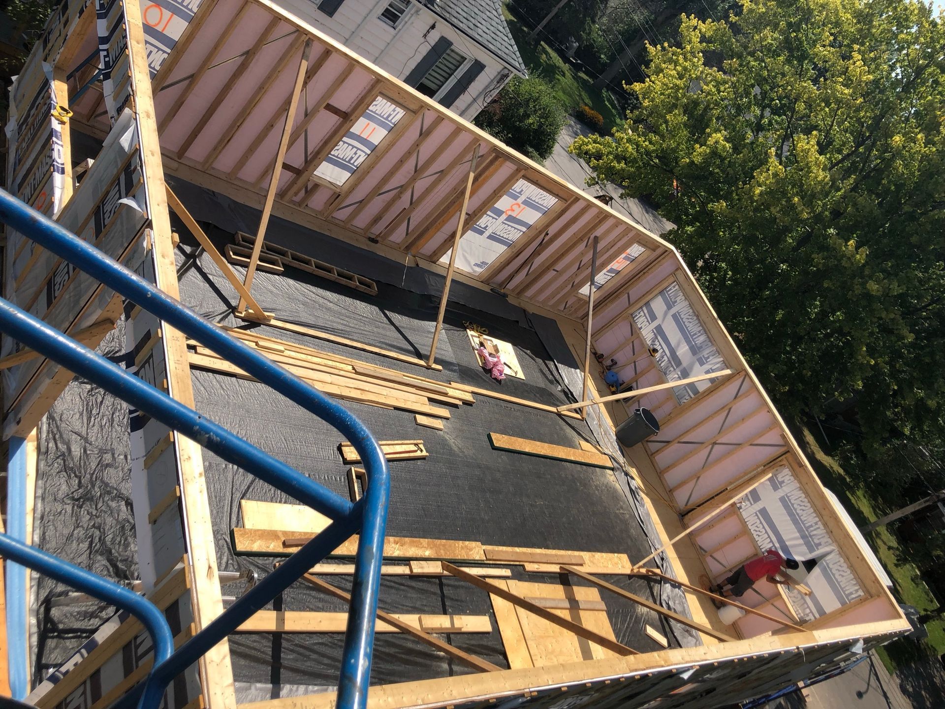 Construction de toiture avec charpente en bois, isolation et couverture noire. Rambarde bleue au premier plan.