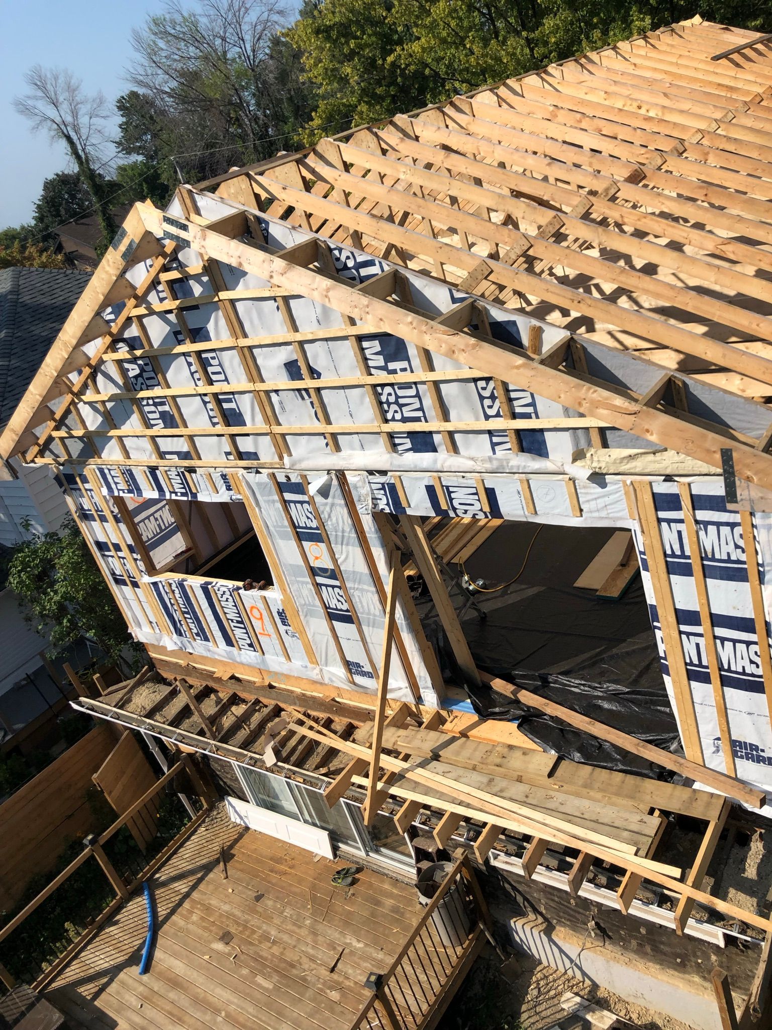 Maison en bois en construction ; la charpente apparente, les chevrons de la toiture et le revêtement sont visibles.
