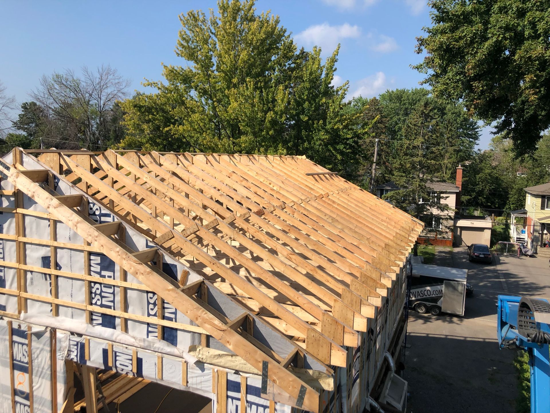 Construction de la toiture d'un bâtiment avec charpente et chevrons en bois ; vue extérieure par temps ensoleillé.