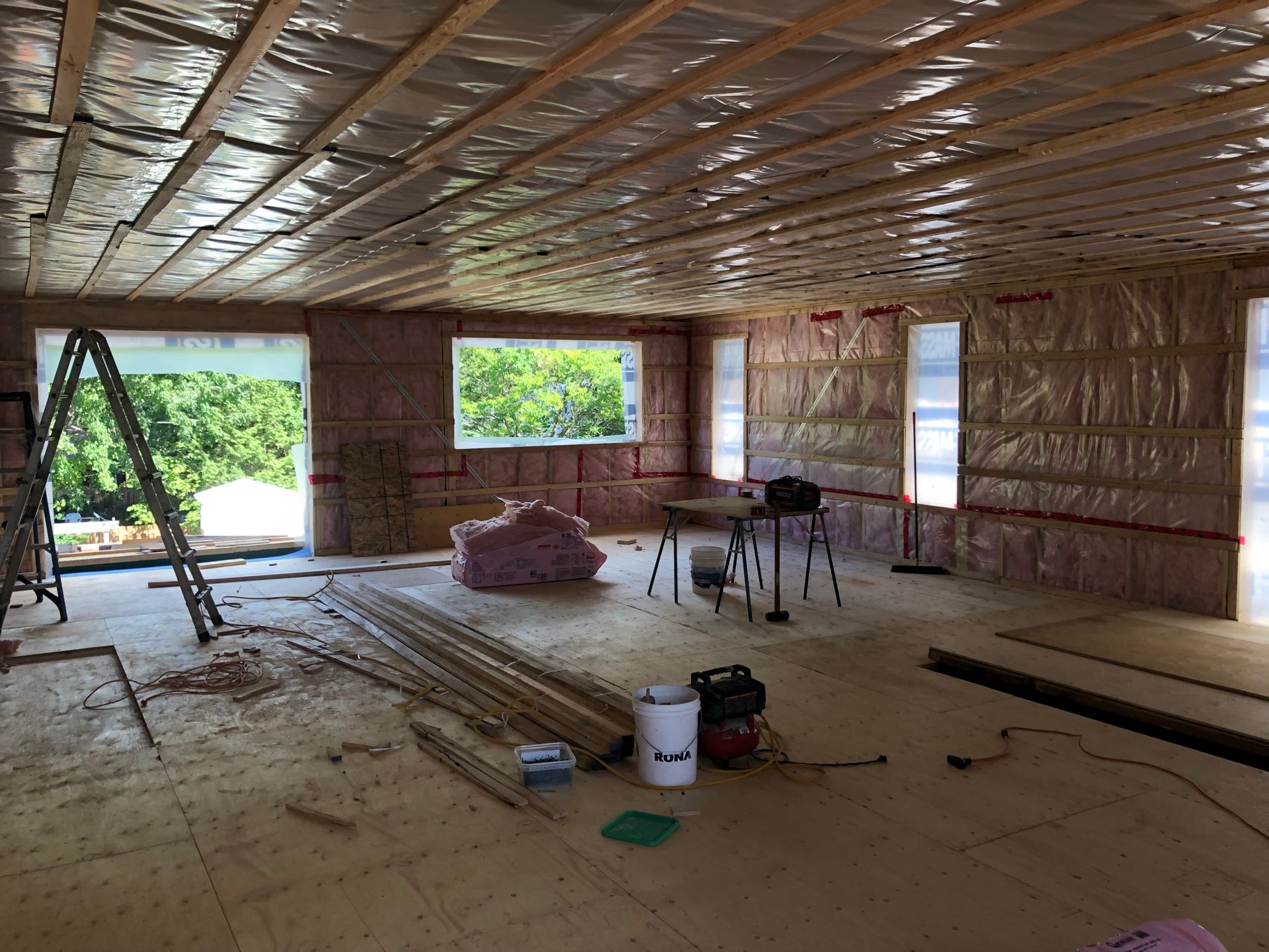 Aménagement intérieur d'une pièce : murs et plafond isolés, fenêtres en place, bois et outils éparpillés.