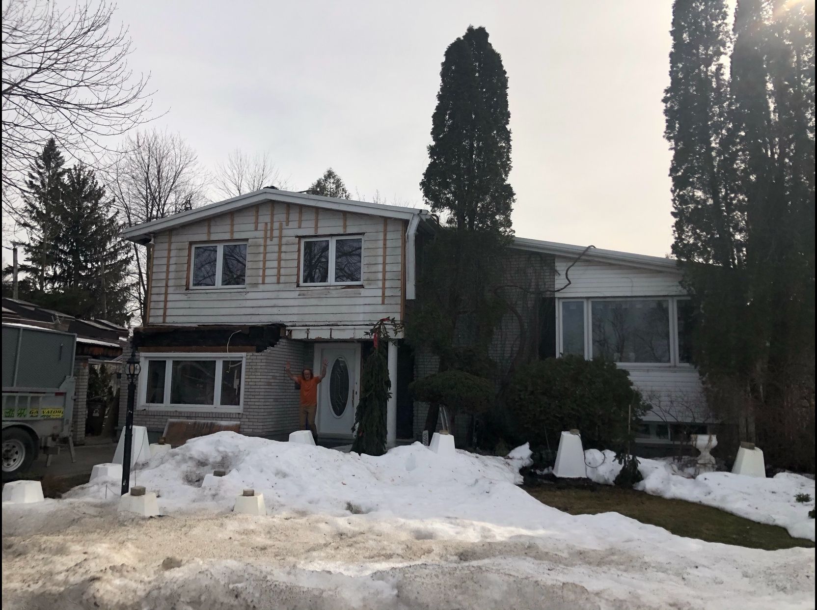 Maison à deux étages au bardage patiné par le temps, recouverte de vigne vierge, partiellement dissimulée par la neige fondante.