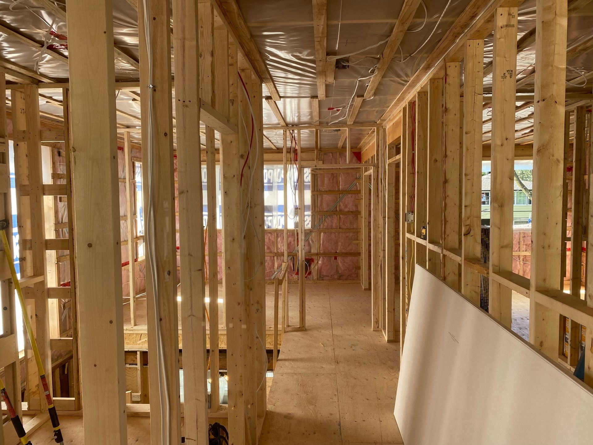 Intérieur d'un bâtiment en construction ; ossature bois pour les murs et le plafond, isolation visible, plaques de plâtre inclinées.