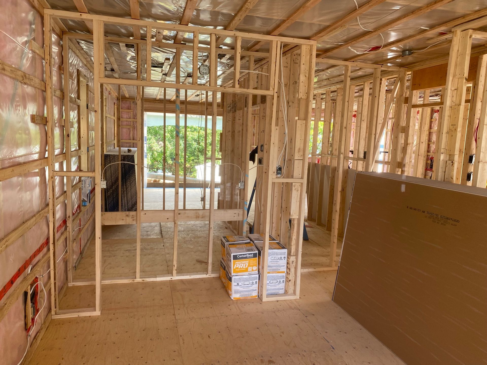 Ossature intérieure d'une pièce en construction avec montants en bois apparents. Isolation et plaque de plâtre visibles.